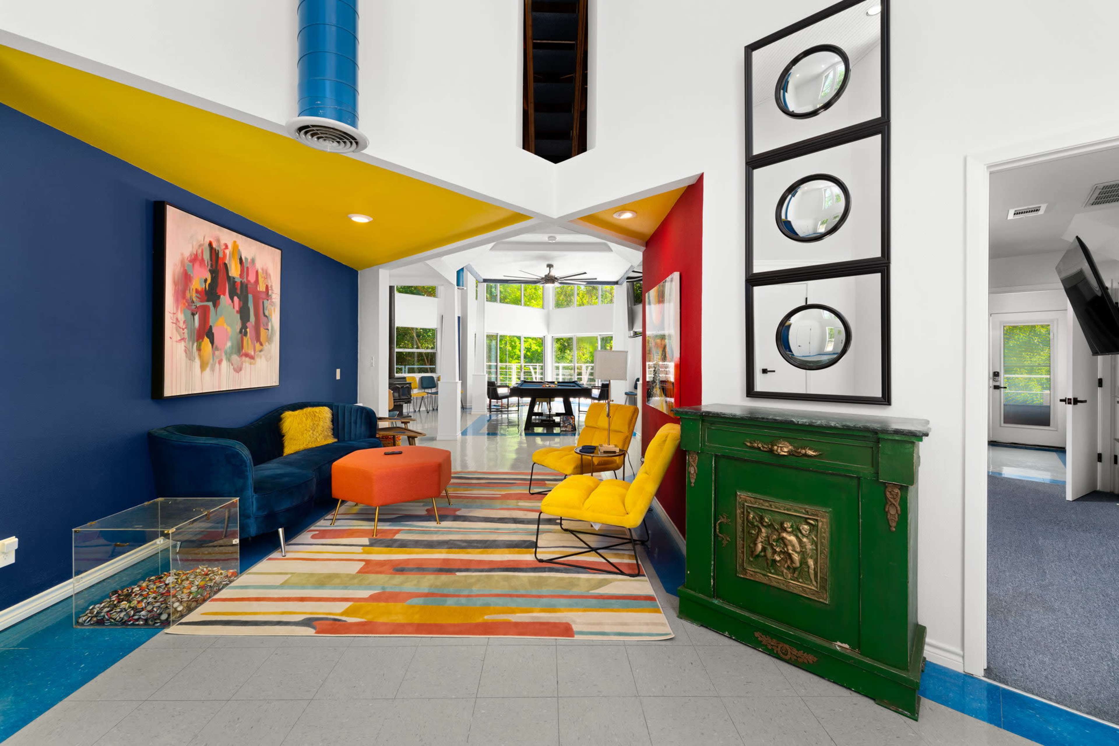 A brightly colored living space with blue, yellow, and red walls, a variety of seating options, and a striped rug.