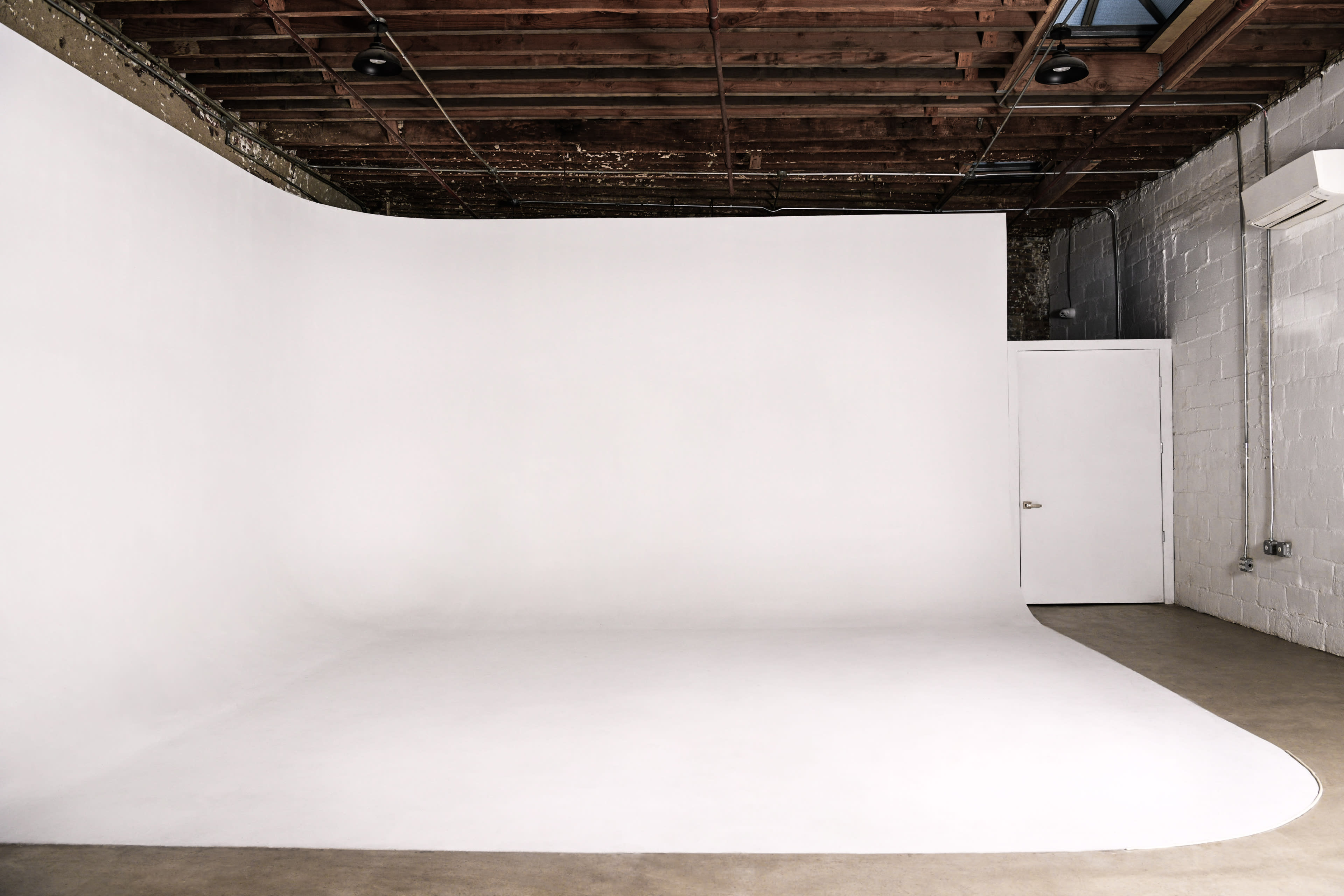 The image shows a minimalist photography studio featuring a seamless white backdrop and a door on one side.