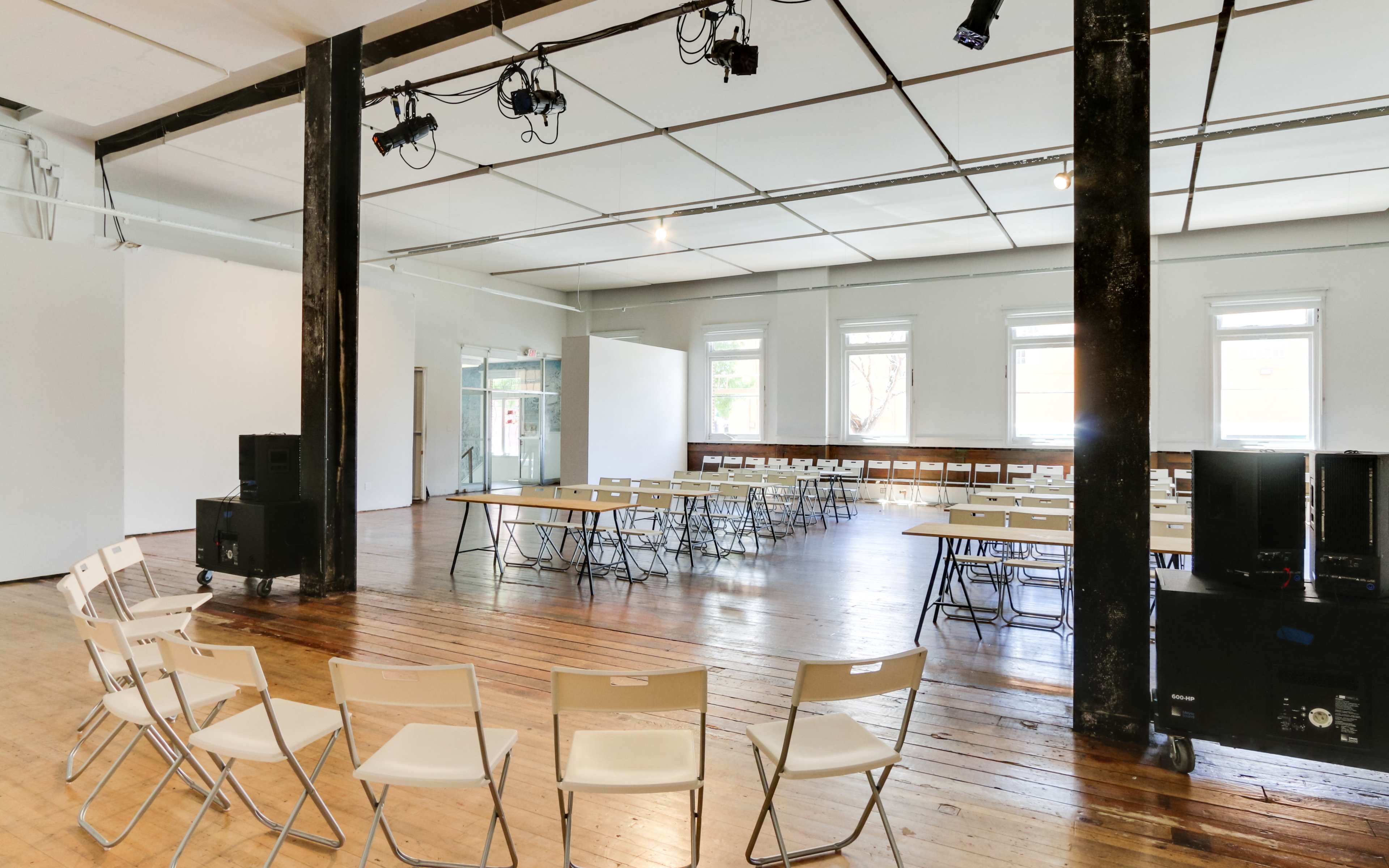 An empty event space with rows of folding chairs facing a section of tables and a sound system in the corner.