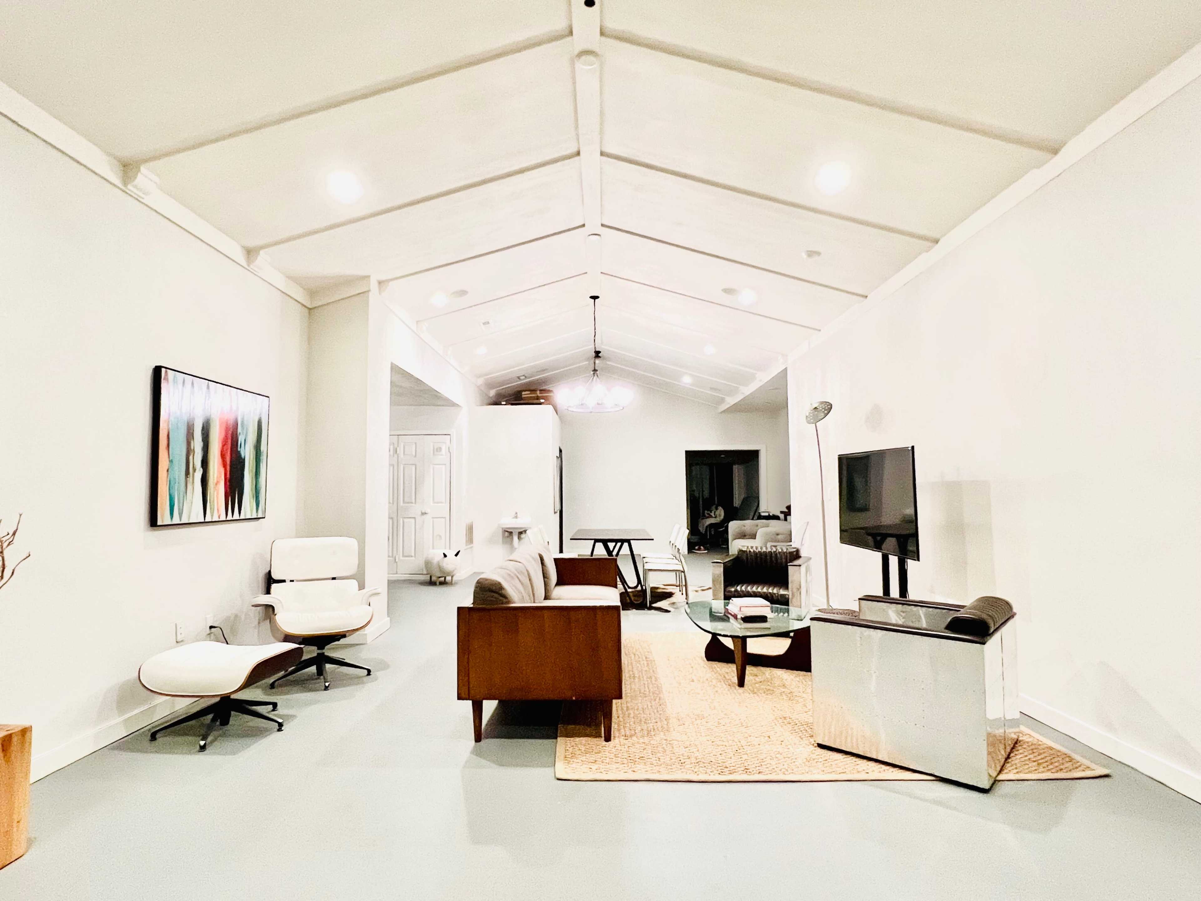 A spacious living area with a high ceiling, featuring a modern seating arrangement, a television, and a minimalist decor scheme.
