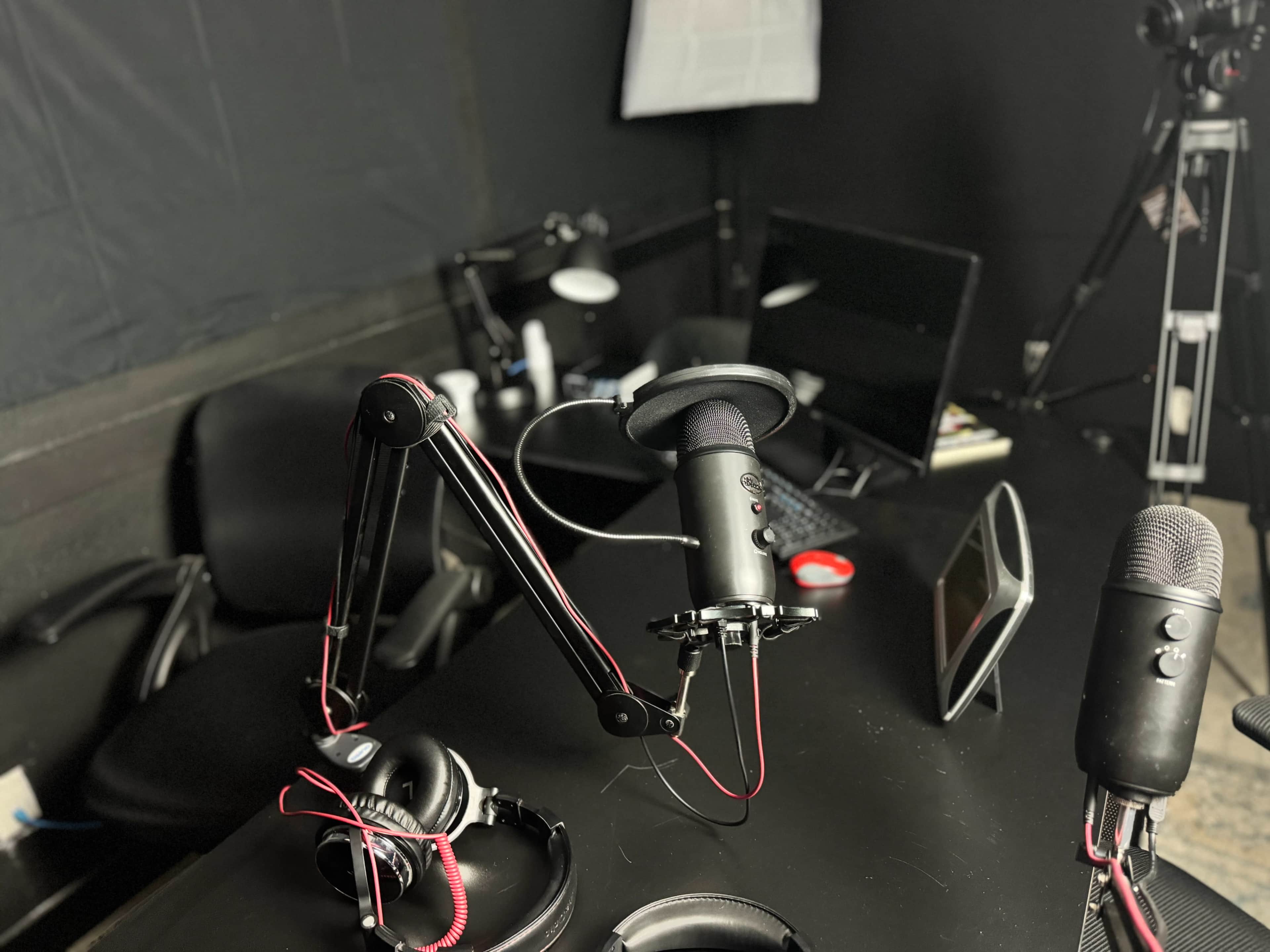 The image shows a recording studio setup with microphones, headphones, and a computer monitor on a black table.