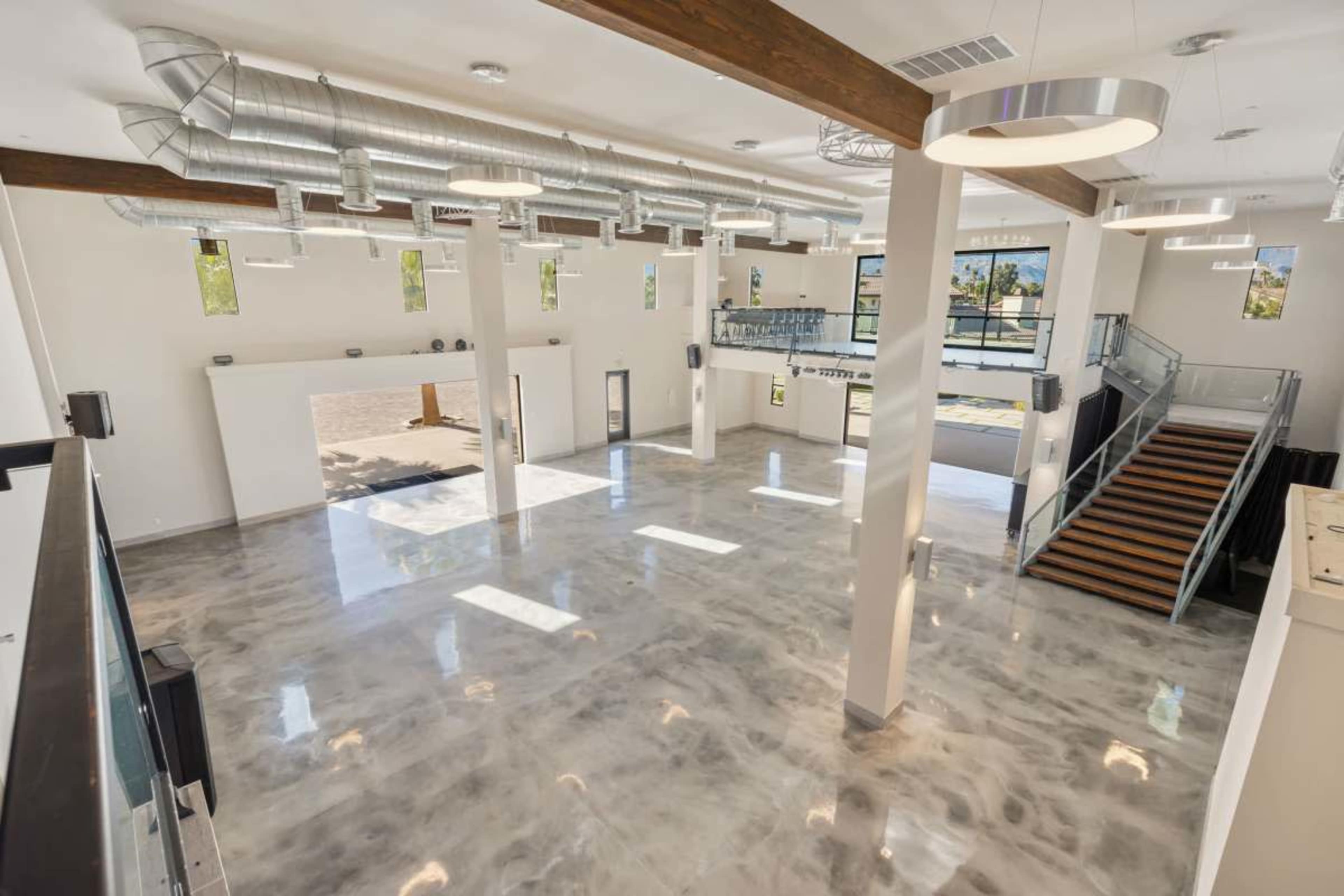 The image shows a spacious, modern commercial interior with polished concrete floors, high ceilings, and large windows allowing natural light.