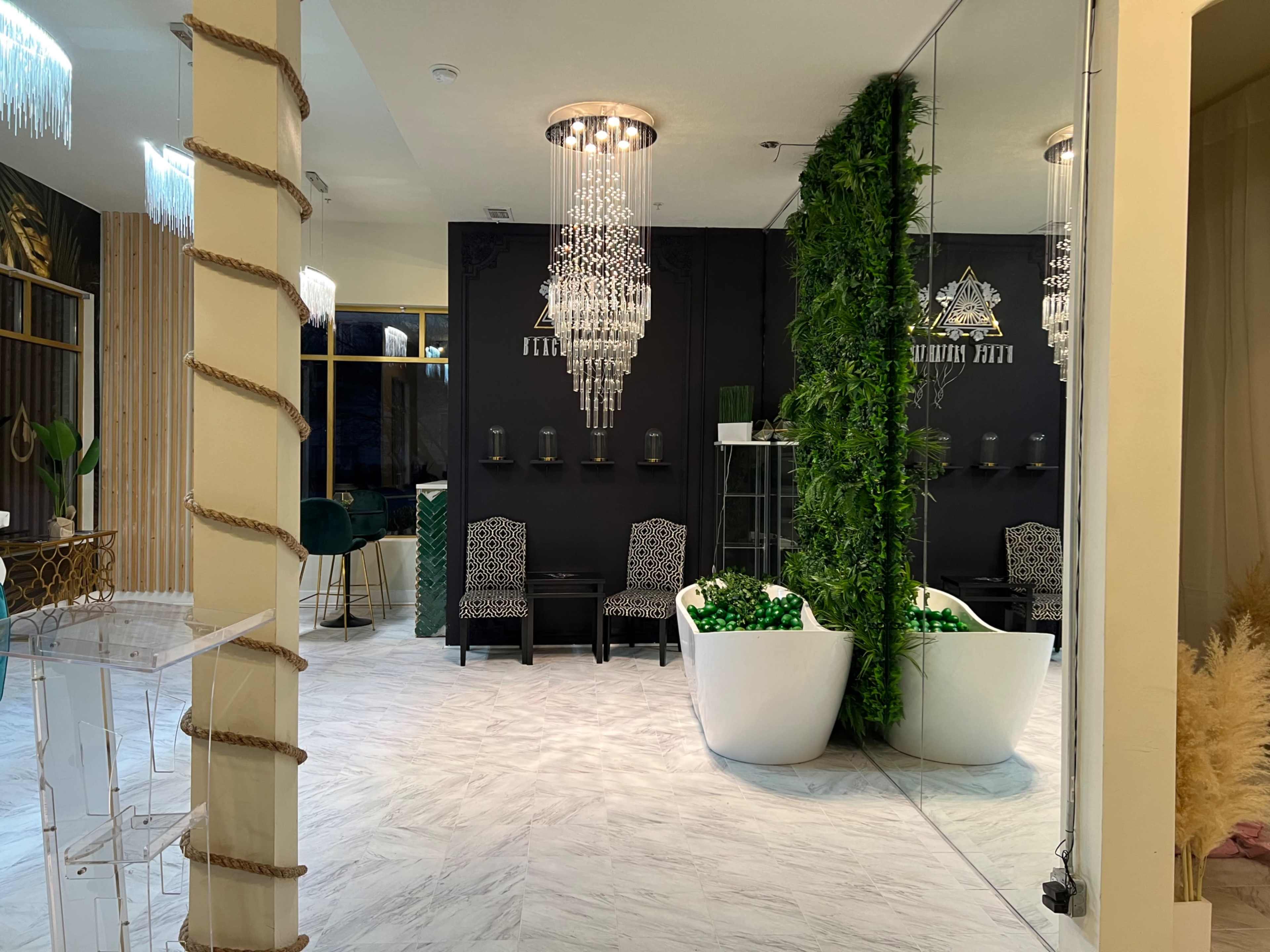 A modern interior space with two white planters filled with greenery, black accent walls, and elegant chandeliers.