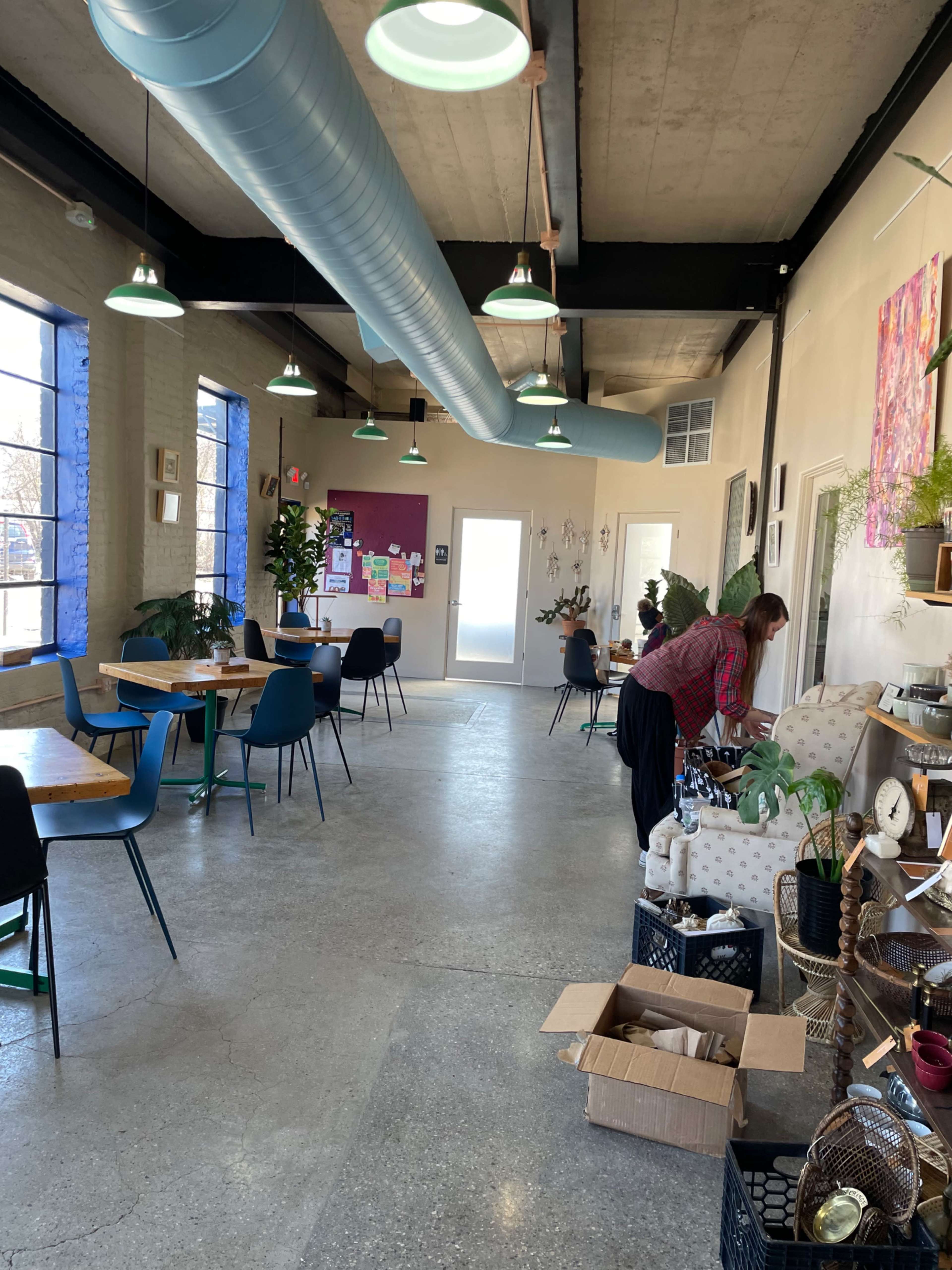 A person arranges items on a table in a spacious, well-lit cafe featuring blue and green decor elements.