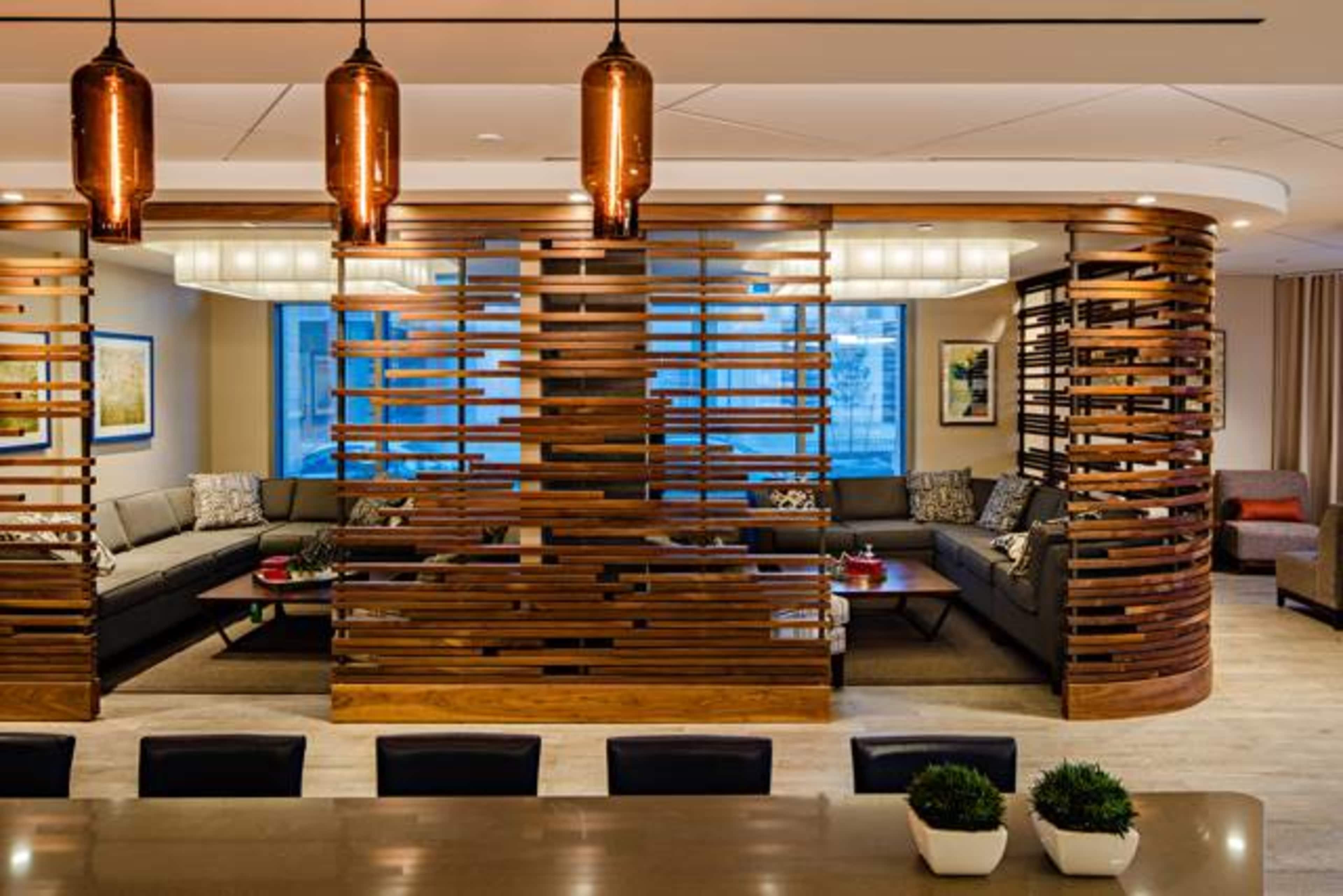 A modern lounge area separated by a wooden slatted partition, featuring comfortable seating and pendant lighting.