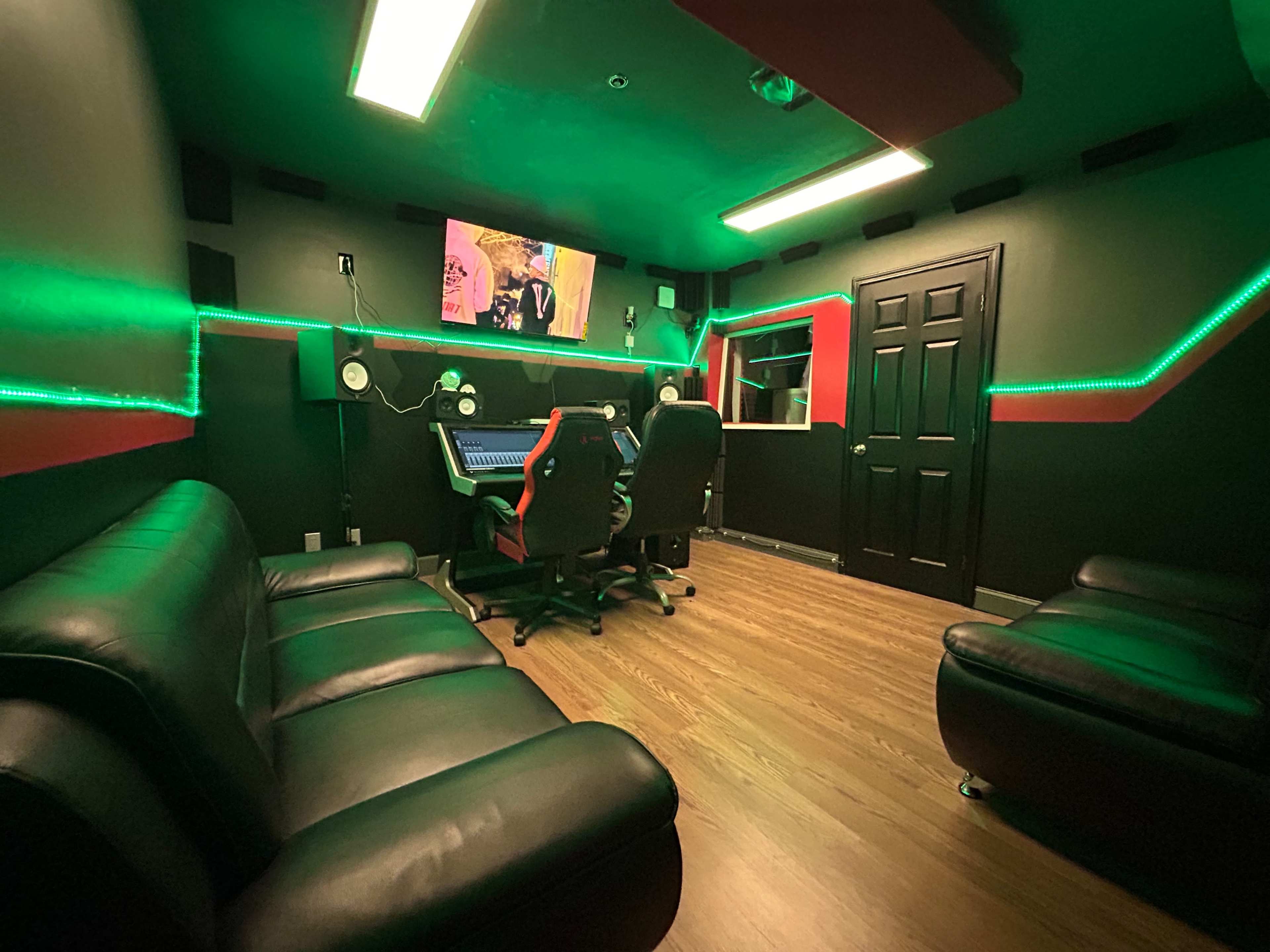 The image shows a recording studio with two black leather sofas, a mixing console, and green LED lights illuminating the walls.