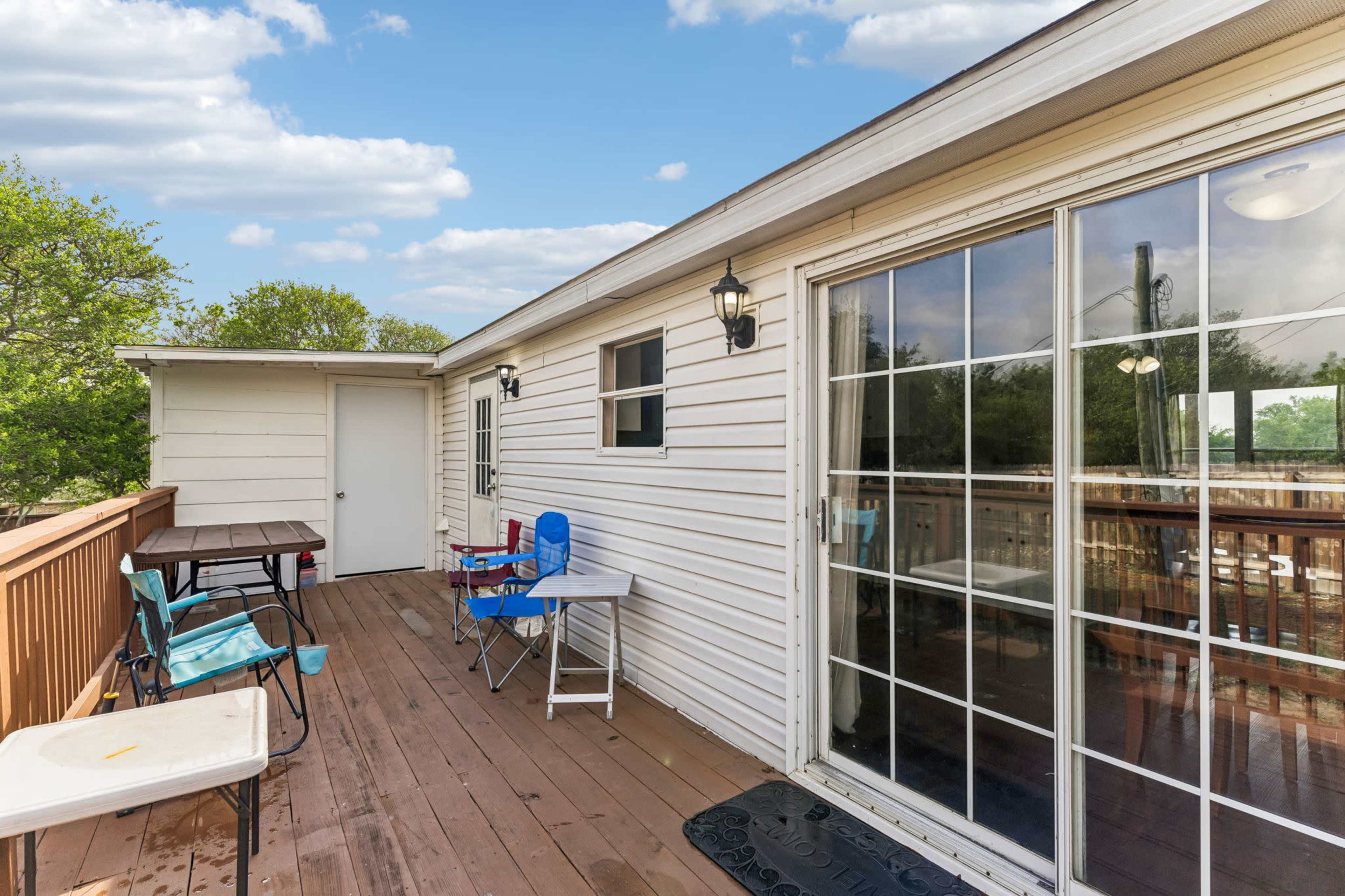 The image shows a wooden patio with several folding chairs and tables, adjacent to a sliding glass door leading into a house.