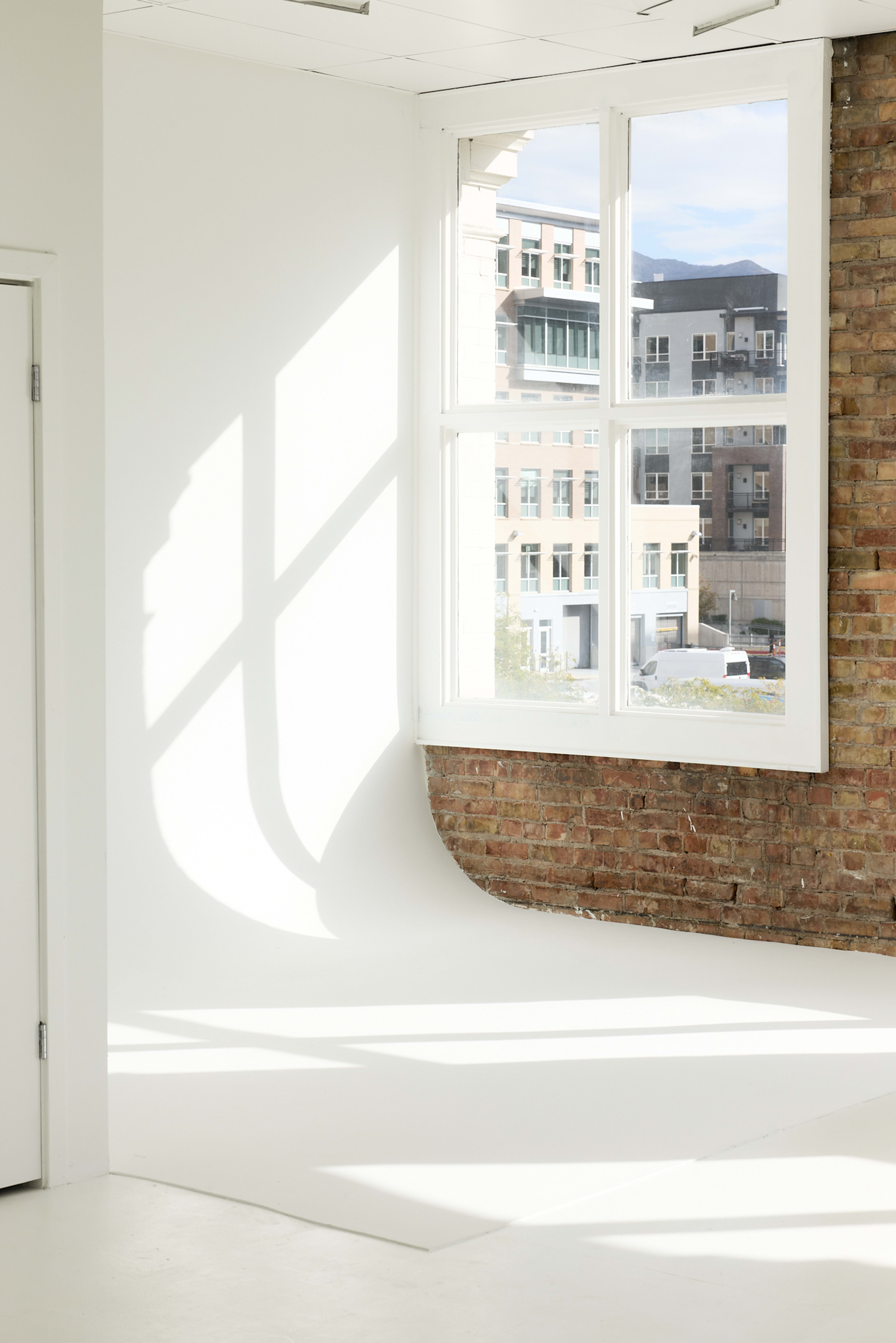 A bright room features a large window with a view of buildings outside and a curved white wall in the corner.