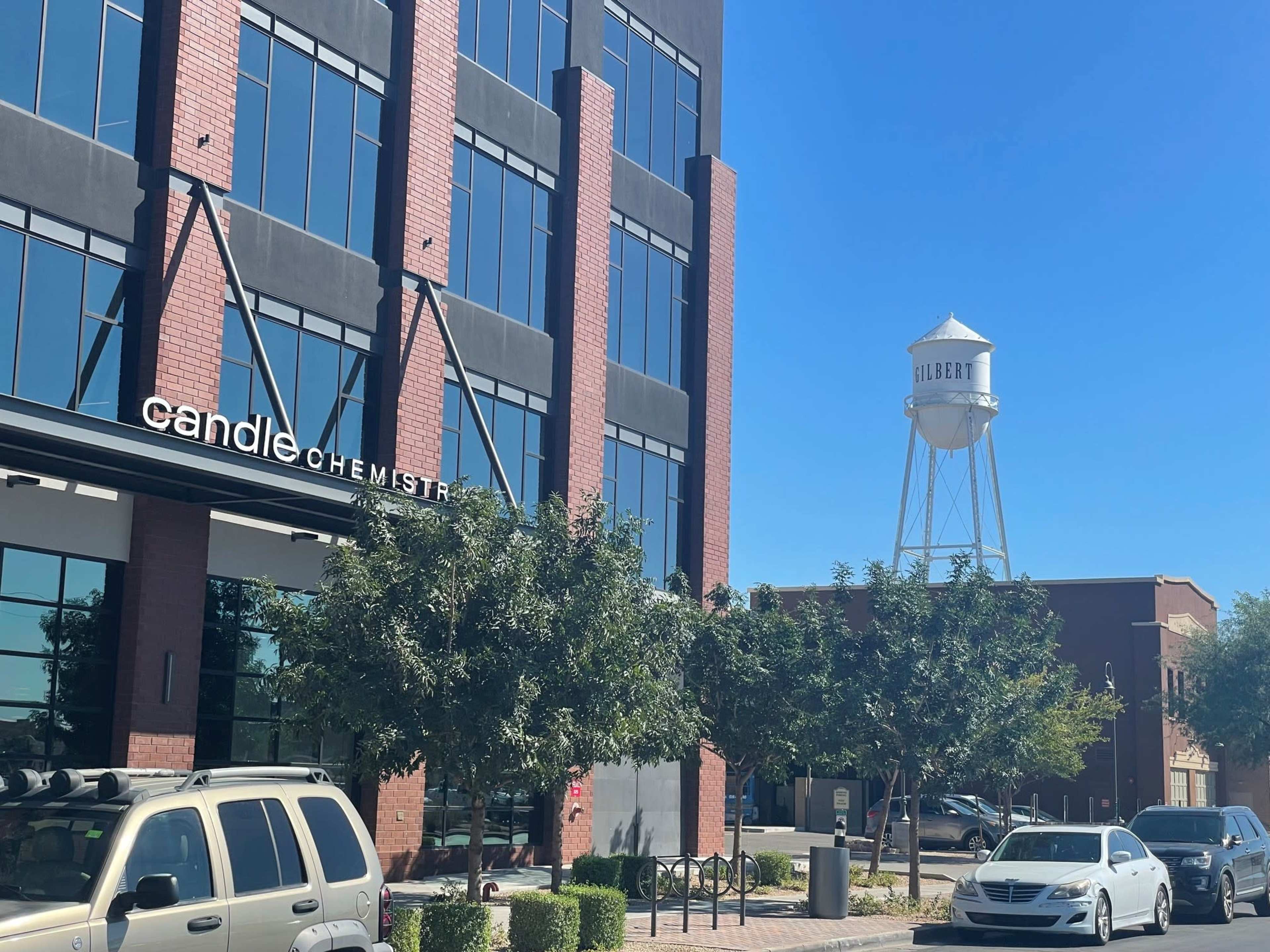 The image shows a modern building with large glass windows, a sign for "candle chemistry," and a nearby water tower labeled "Gilbert."