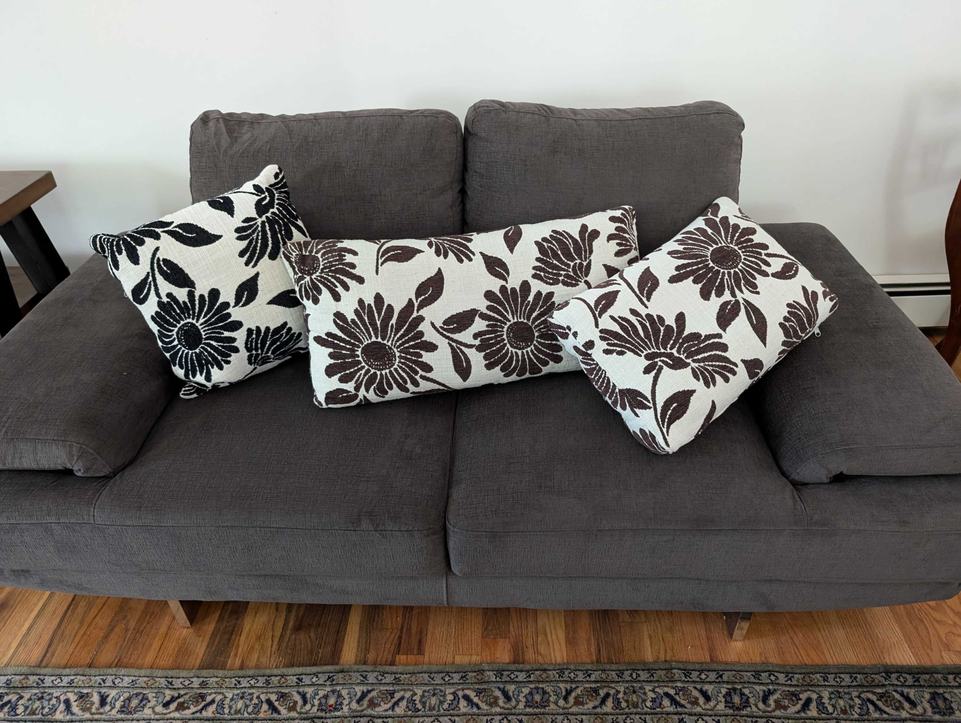 A gray couch is adorned with three decorative pillows featuring black floral patterns.