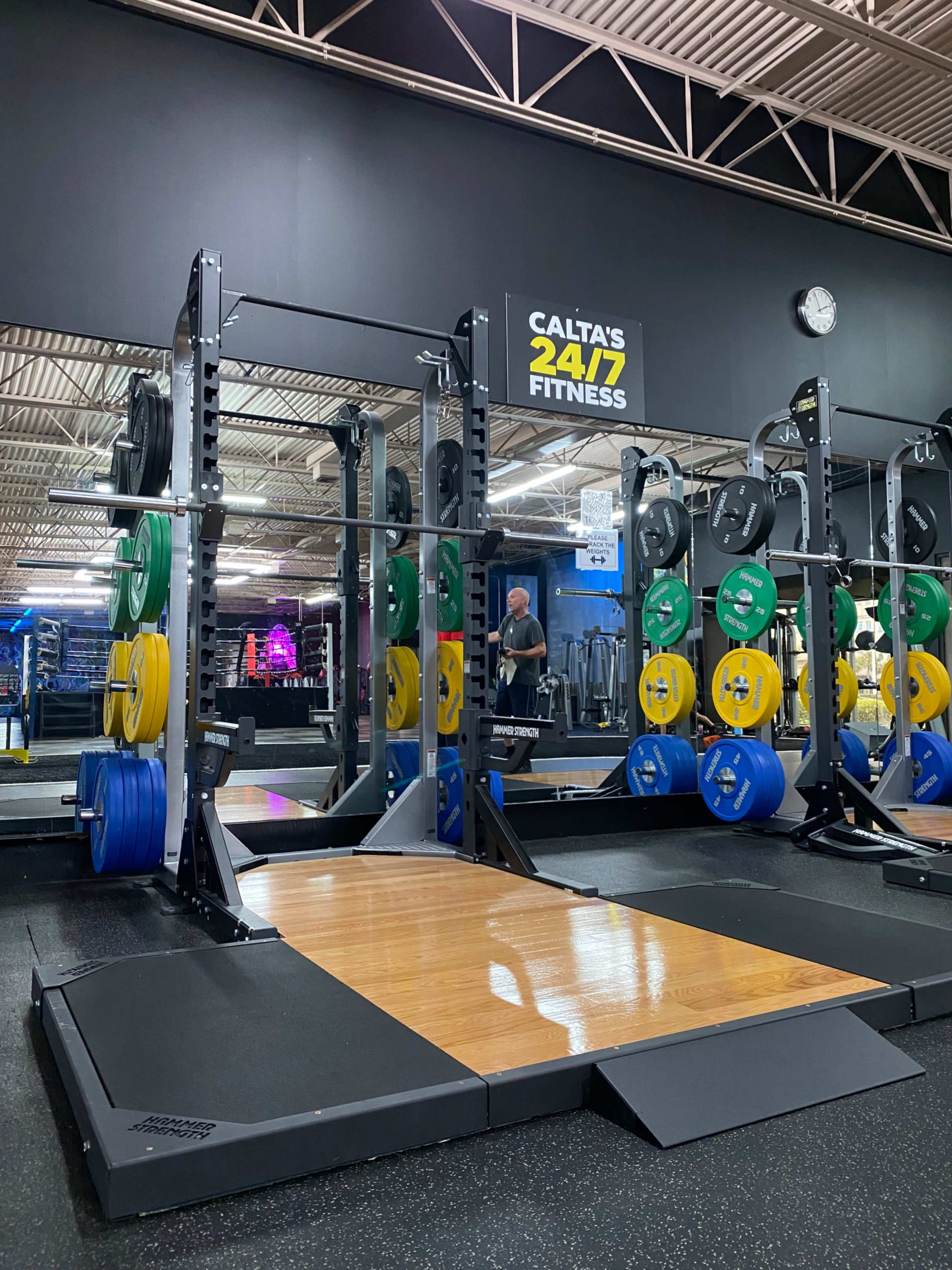 A gym area with a weightlifting platform, surrounded by various color-coded weight plates and exercise equipment in the background.