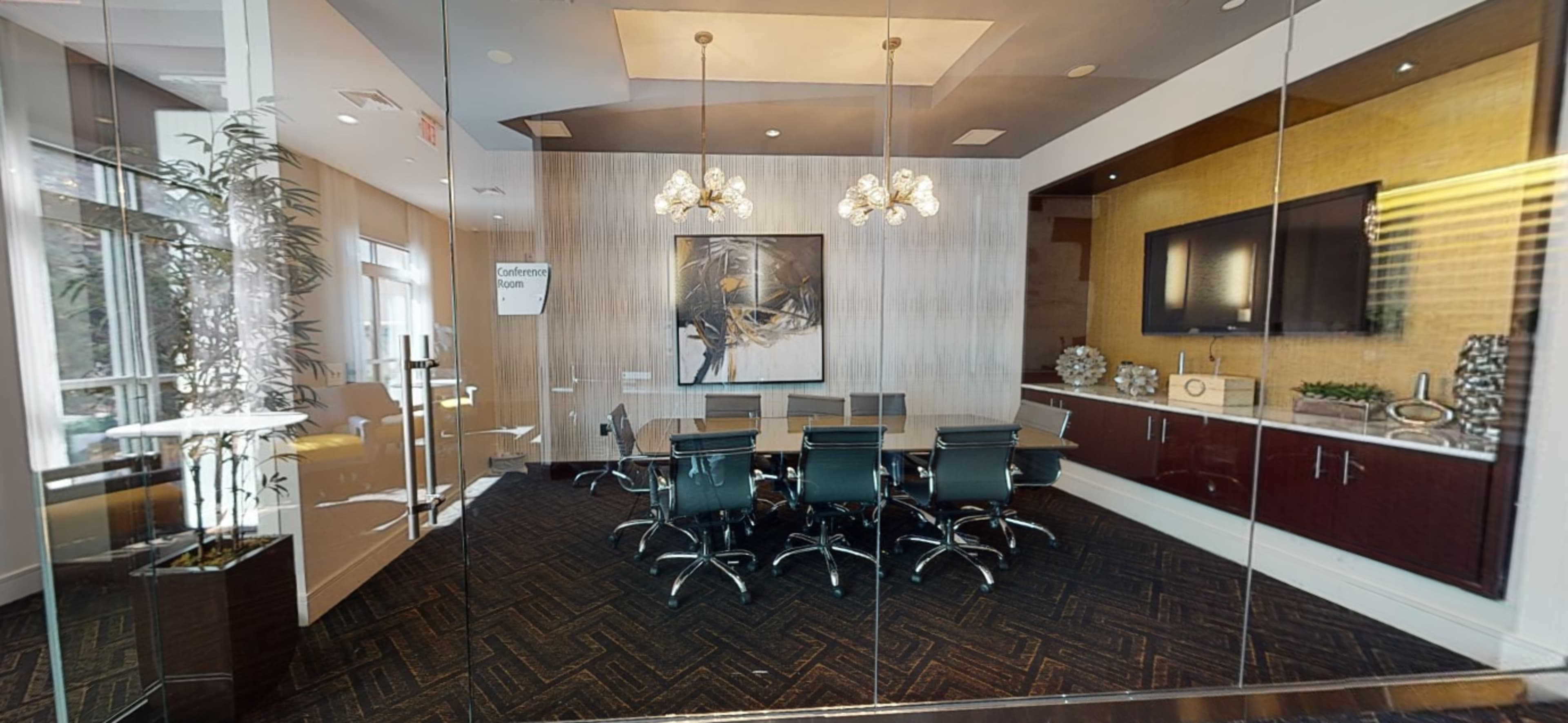 A modern conference room featuring a large table surrounded by black chairs, with a decorative wall and art, illuminated by hanging light fixtures.