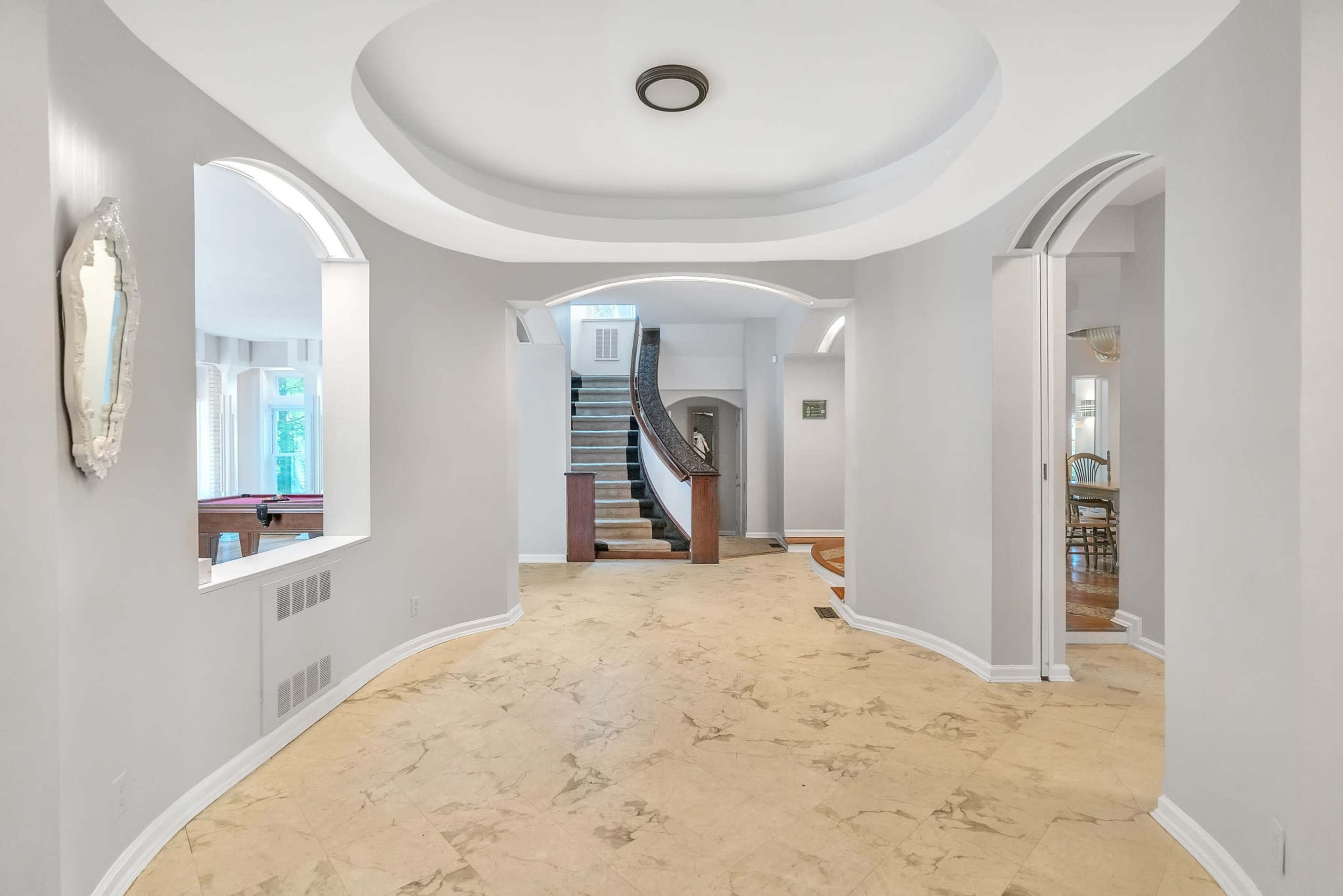 An entryway with a smooth, curved ceiling, featuring arches leading to a staircase and adjacent rooms.