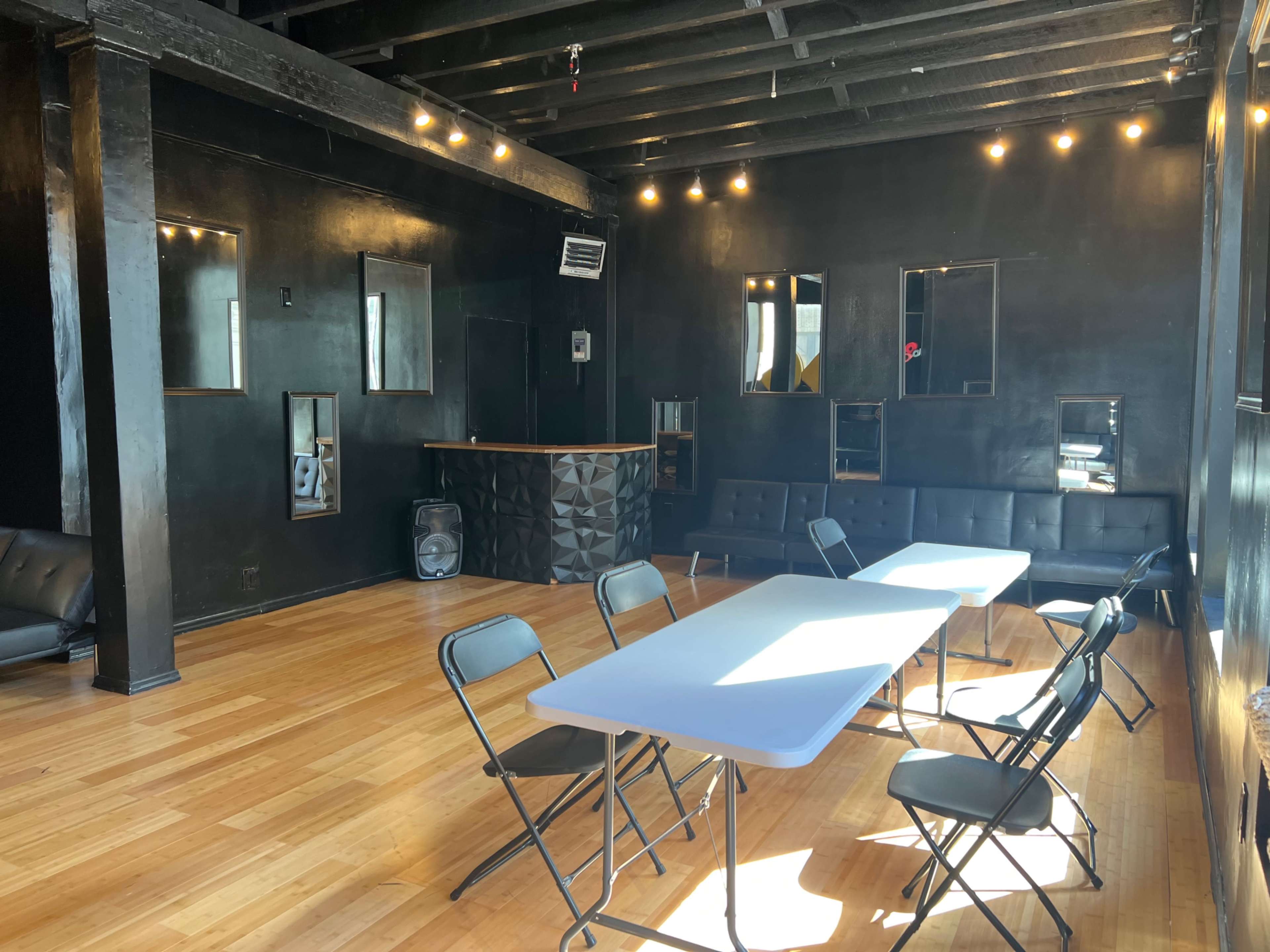A spacious room with black walls, wooden flooring, a bar counter, and several tables and chairs arranged for an event.