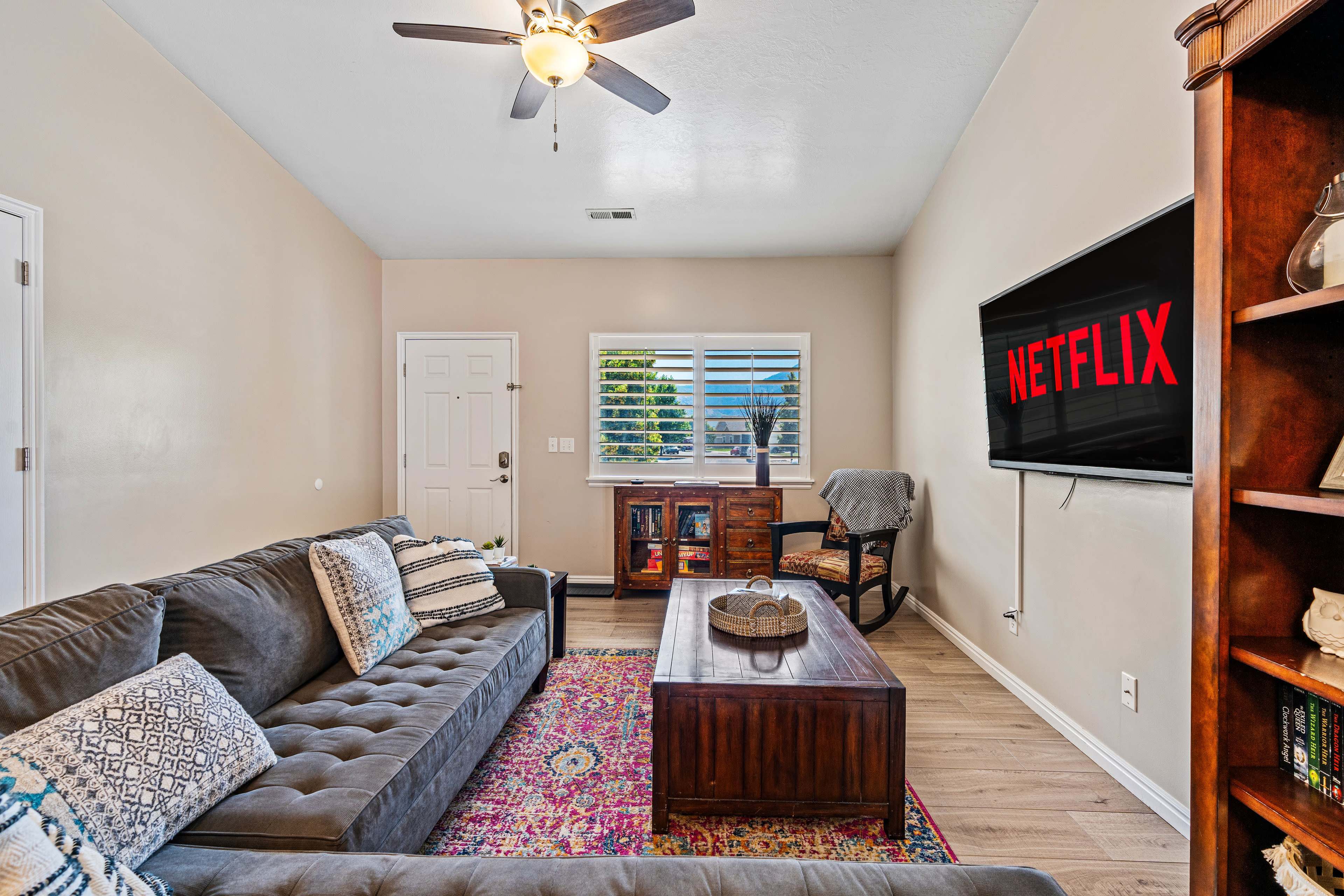 The living room features a gray sectional sofa, a wooden coffee table, and a wall-mounted television displaying the Netflix logo.