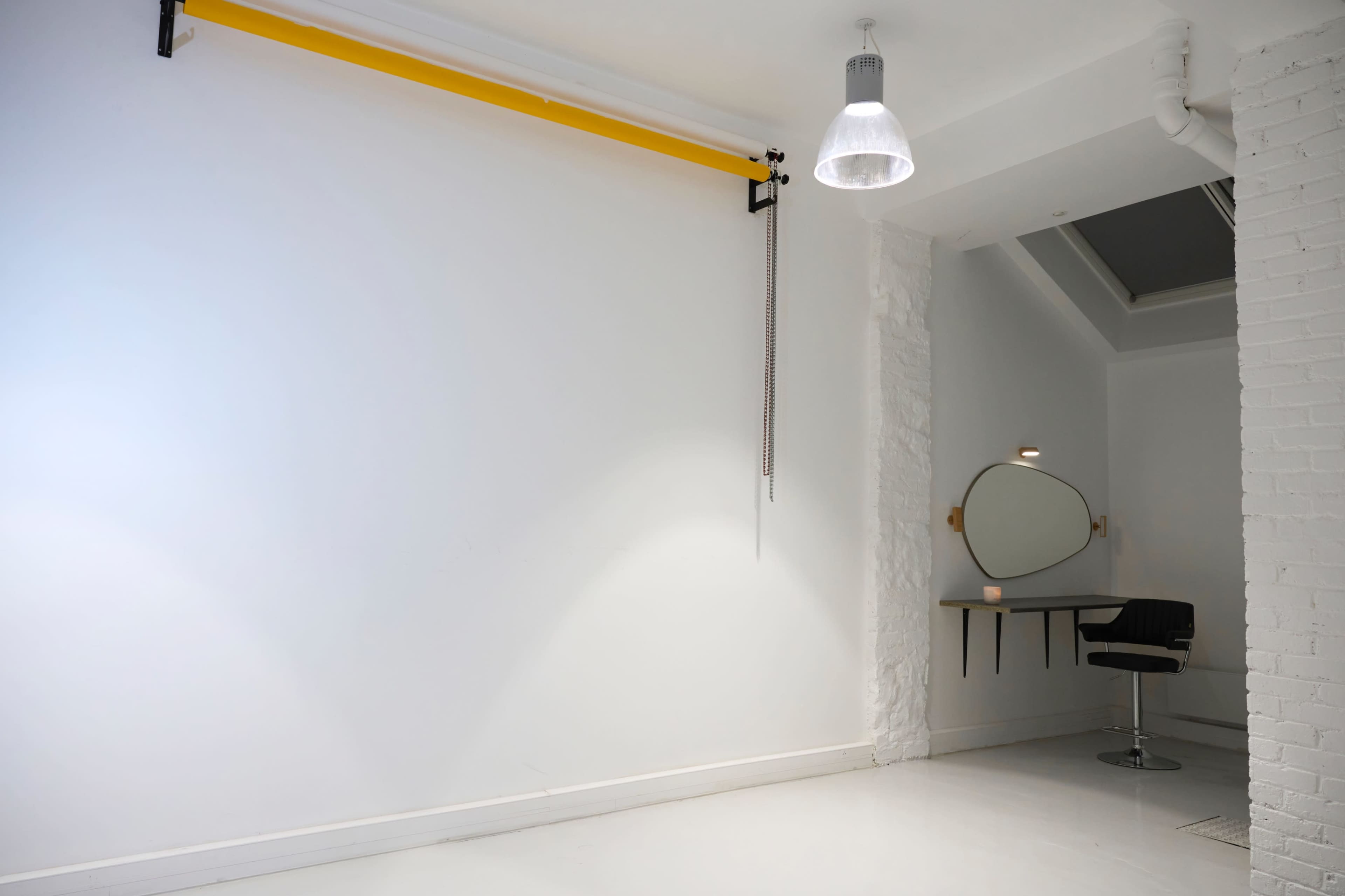 A minimalist interior space with a white wall, a black chair positioned near a circular mirror, and a yellow bar mounted on the wall.
