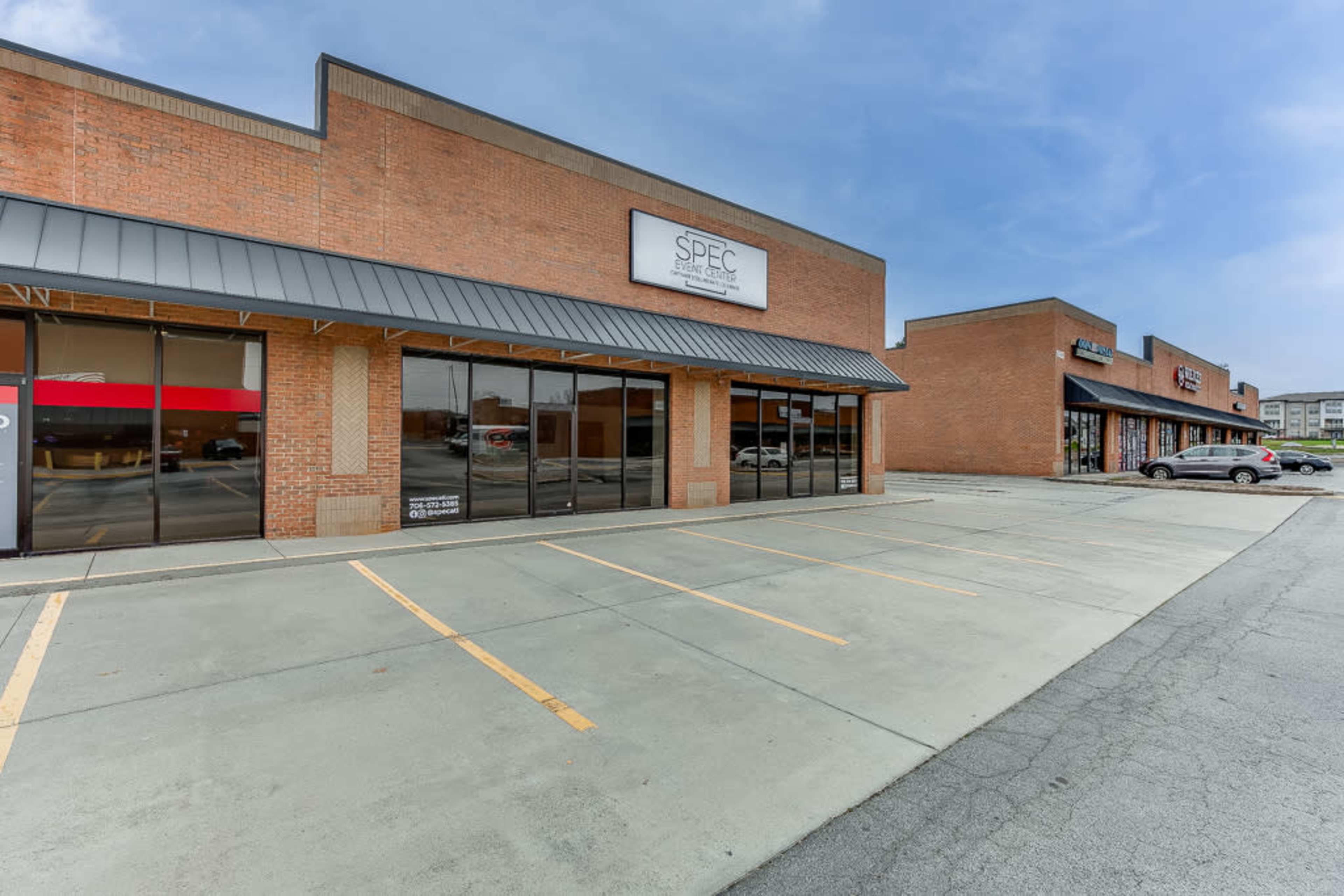 A row of commercial buildings with large windows and parking spaces in front.