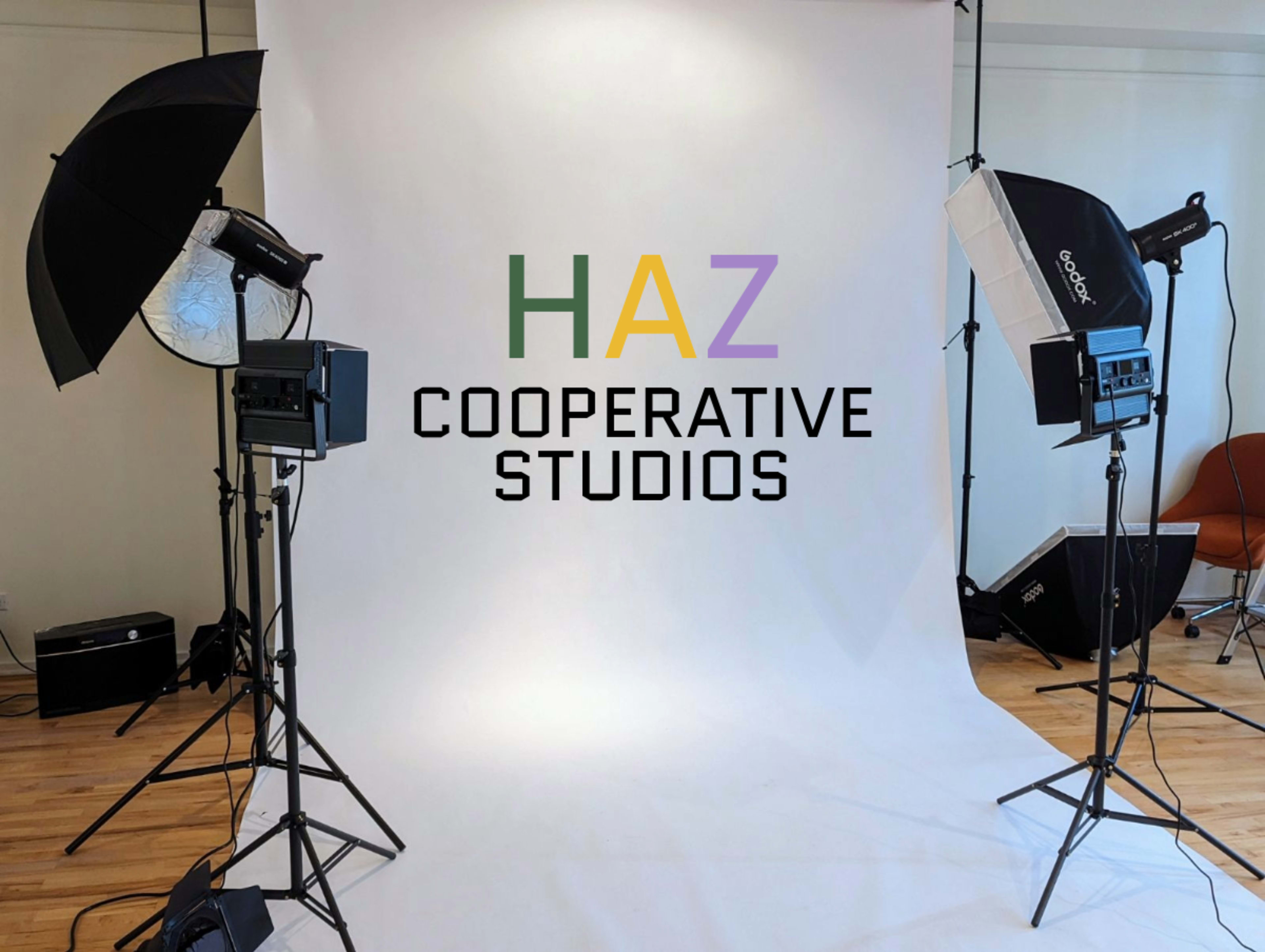 A photography studio setup with lights, softboxes, and a large white backdrop, featuring the text "HAZ COOPERATIVE STUDIOS" in bold letters.