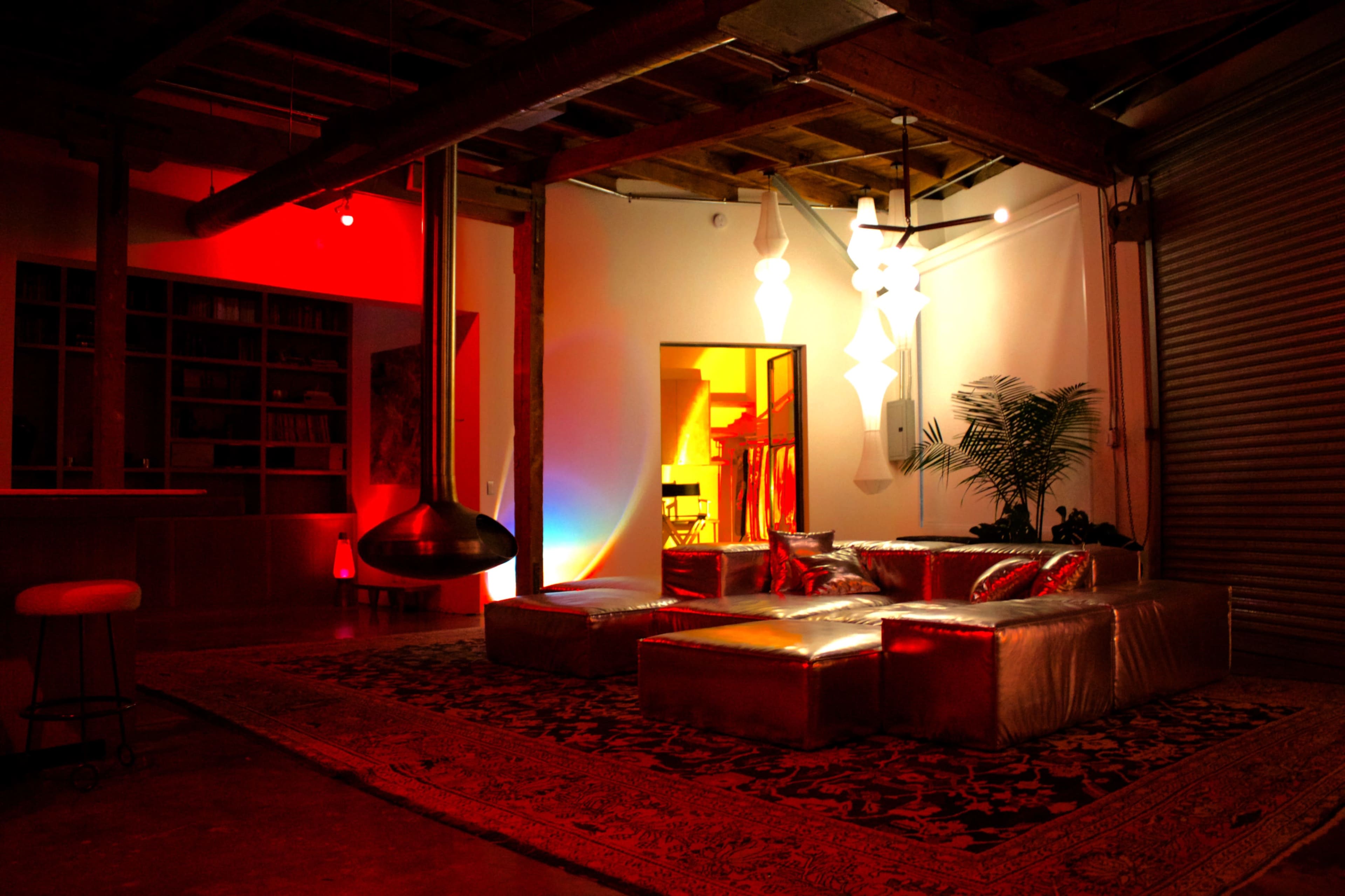 The image shows a spacious loft-style living area with a metallic sofa, colorful lighting, and a modern fireplace.