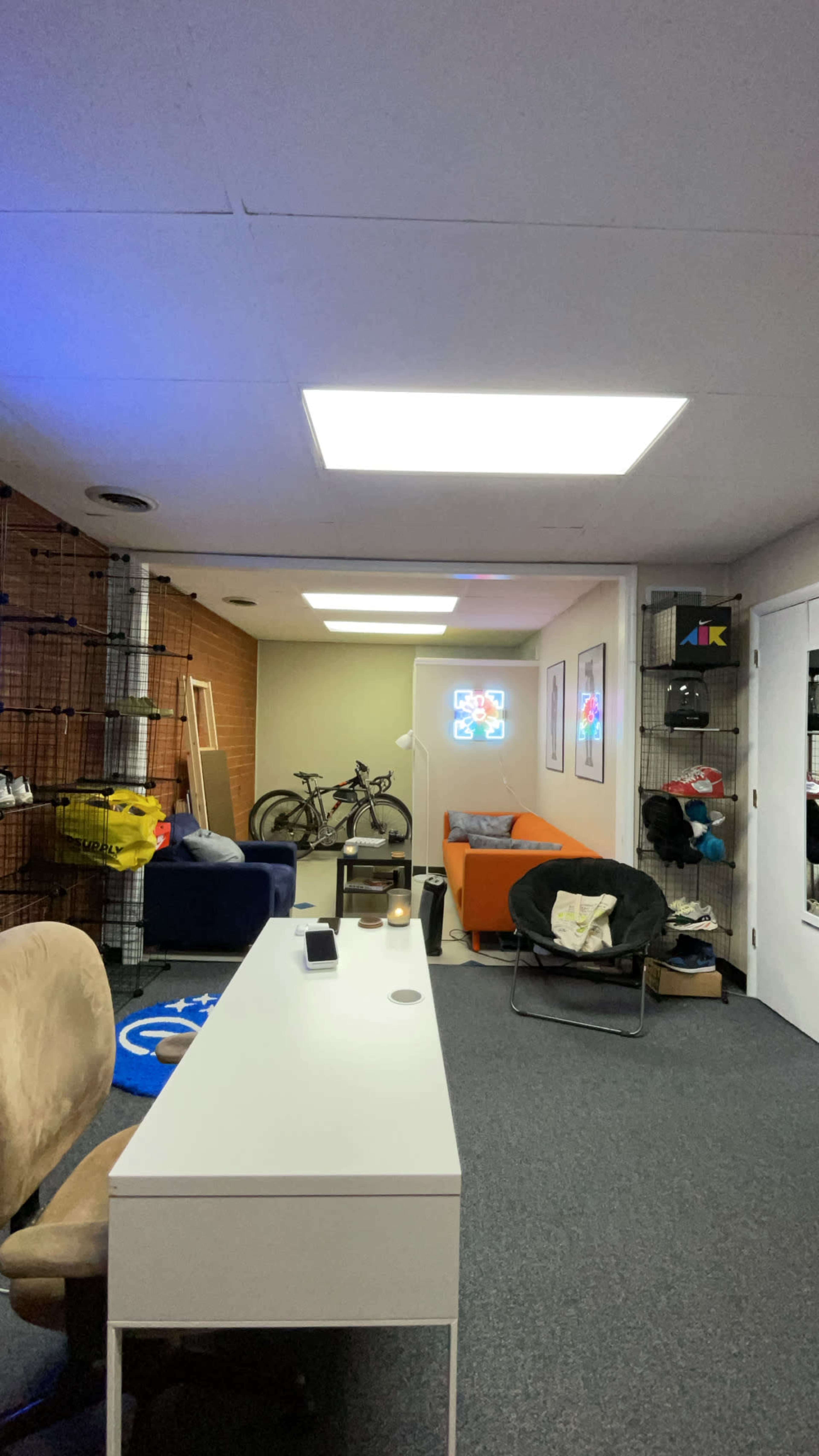 The image shows a well-lit basement room with various seating areas, a desk, and a bicycle leaning against the wall.