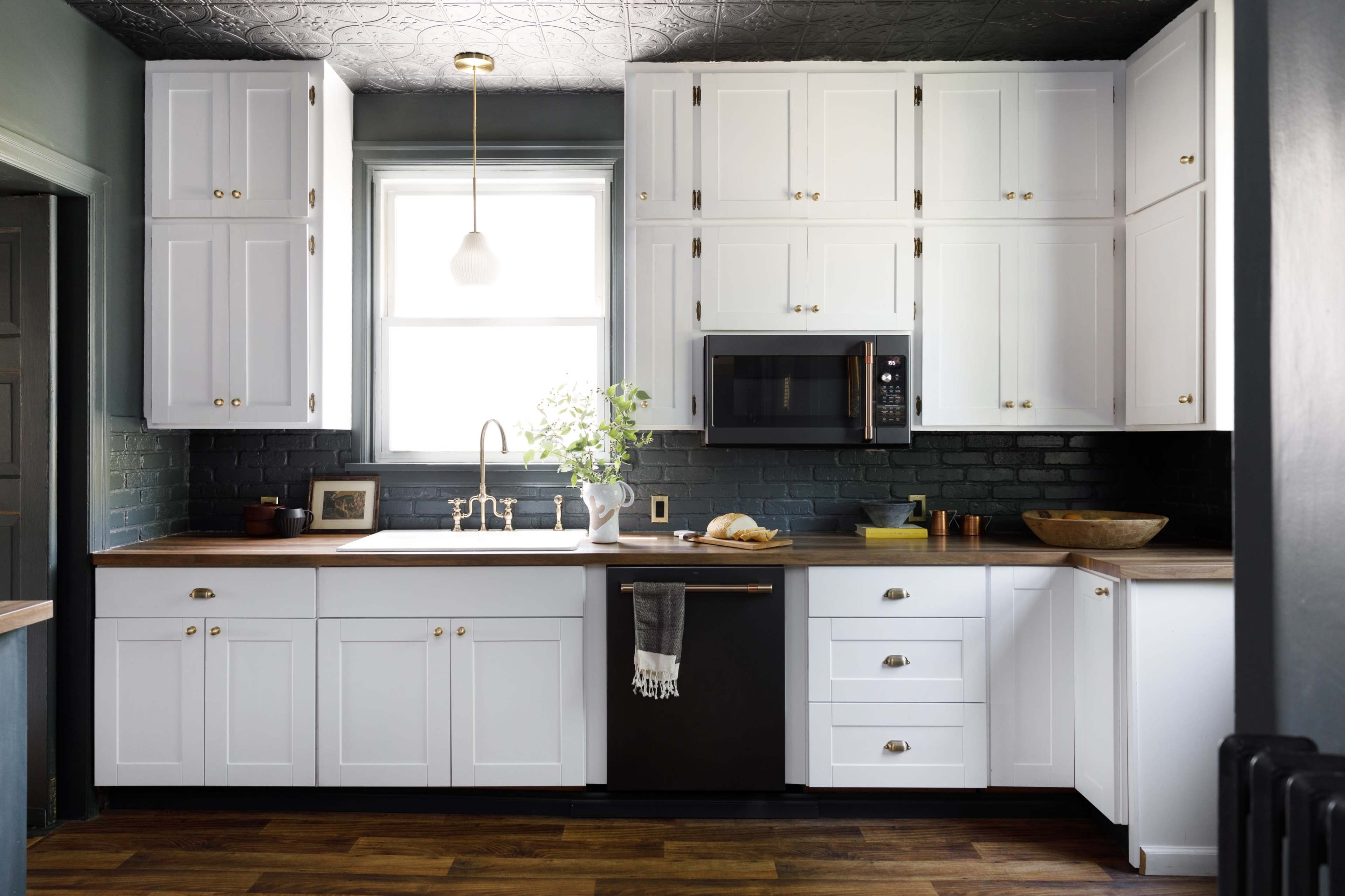 The kitchen features white cabinets, a dark countertop, a stainless steel microwave, and a farmhouse sink with a window above it.