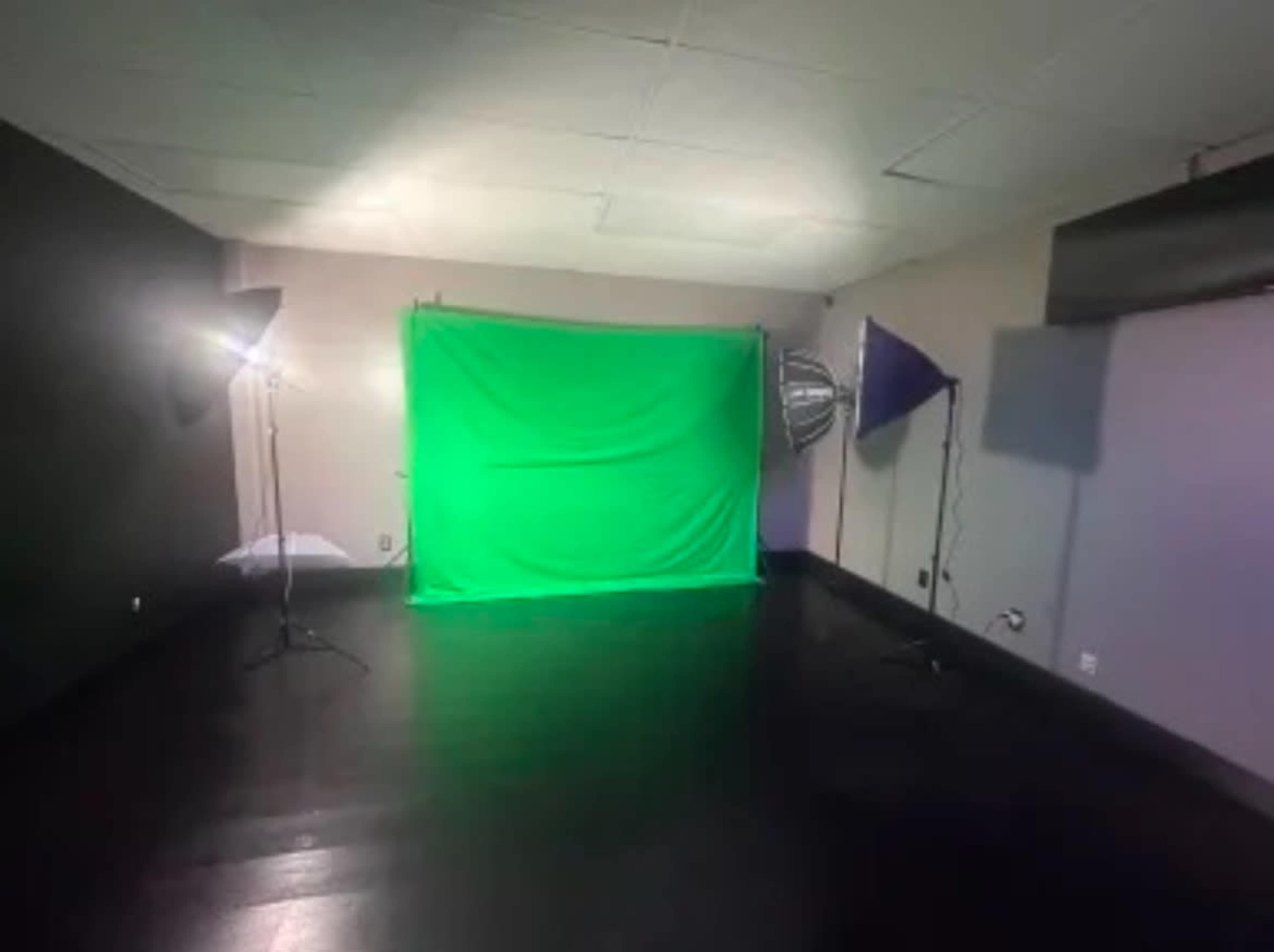 The image shows a small studio space featuring a green screen backdrop, two lighting setups, and a dark floor.