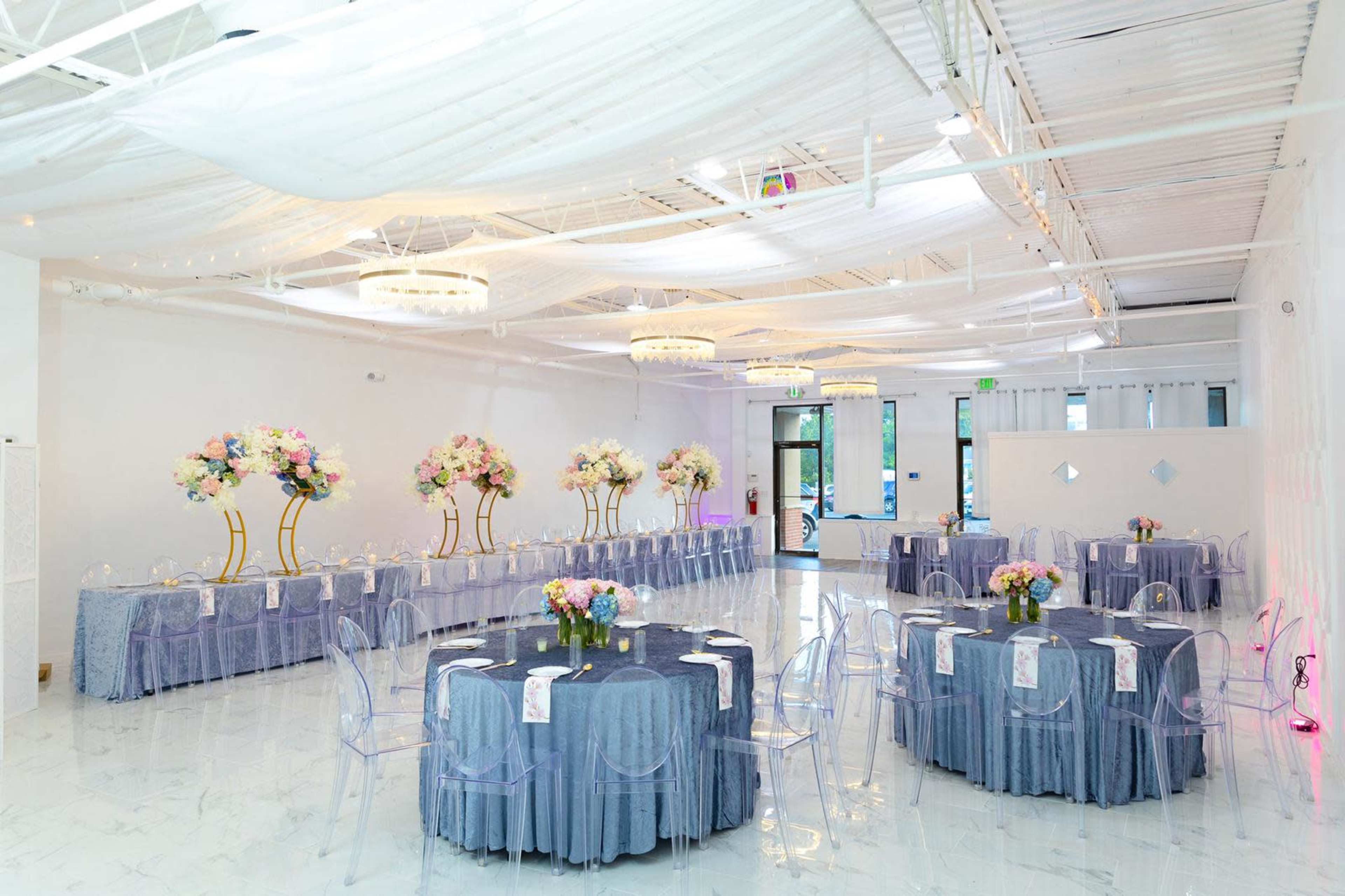 A spacious event venue with round tables set with floral centerpieces and illuminated chandeliers.