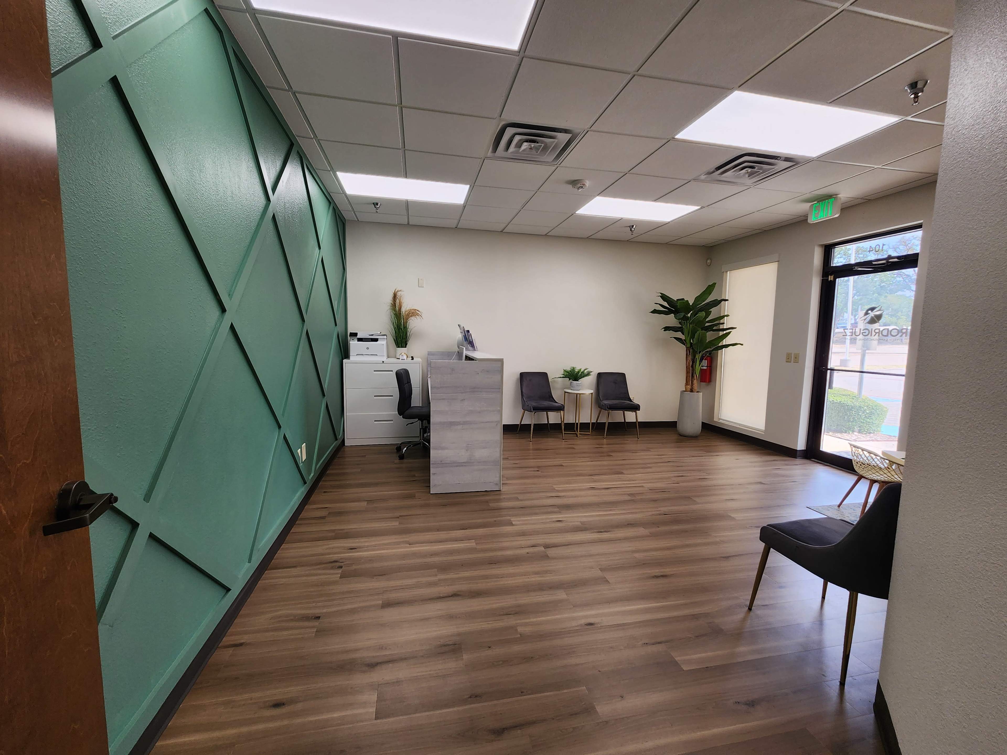 The image shows a modern reception area with a green accent wall, wooden flooring, and minimalist furniture including a front desk and seating.