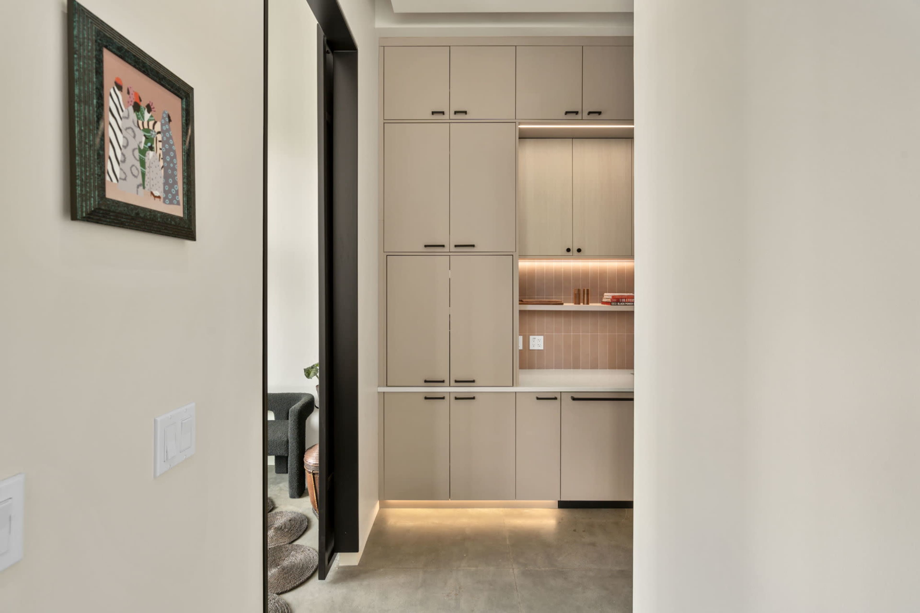 A narrow hallway leading to a modern cabinetry unit with integrated lighting and a framed artwork on the wall.