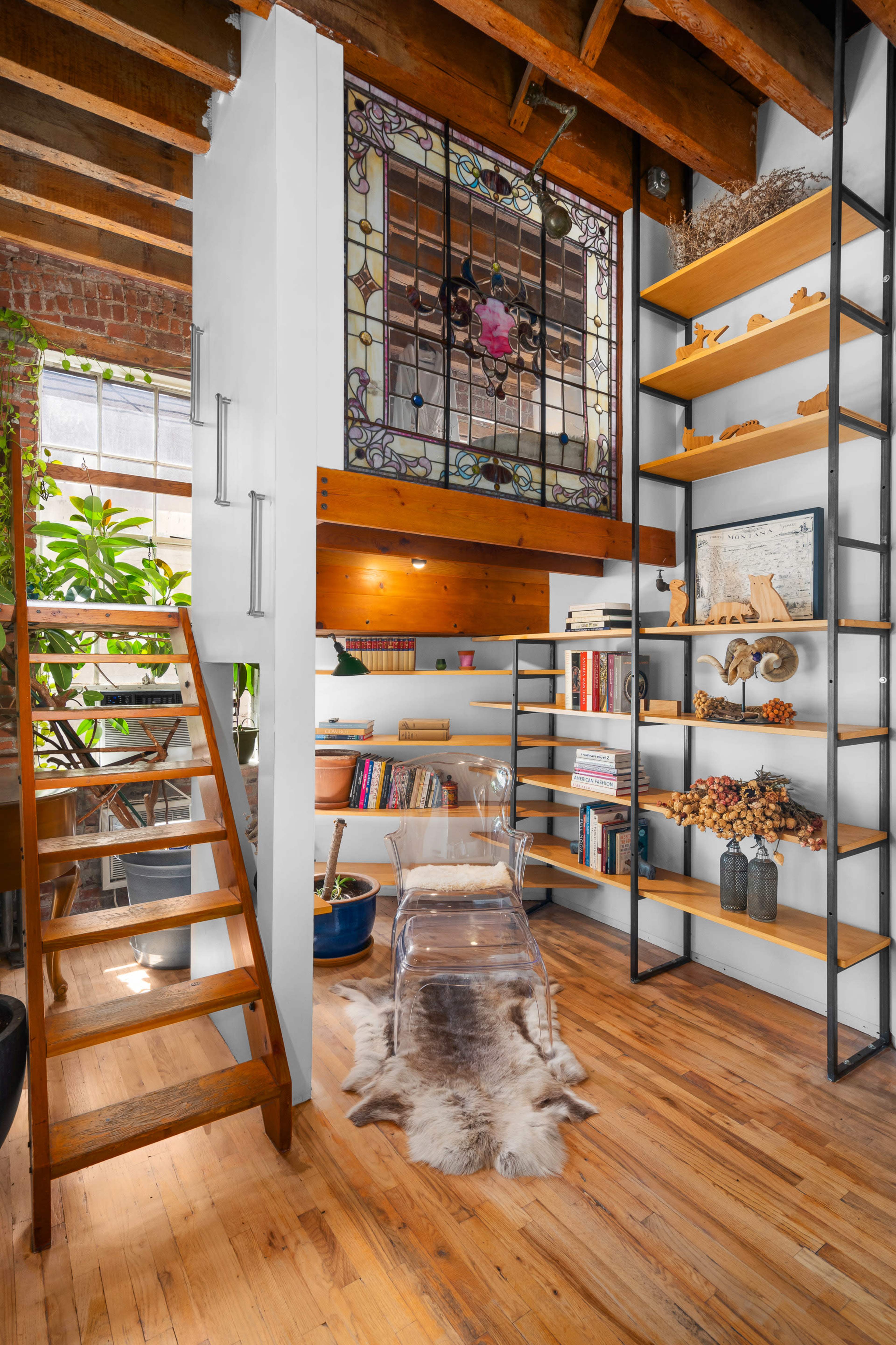 A cozy interior featuring wooden stairs leading to an upper level, a bookshelf lined with various books, and a stained glass window casting colorful light onto the wooden floor.