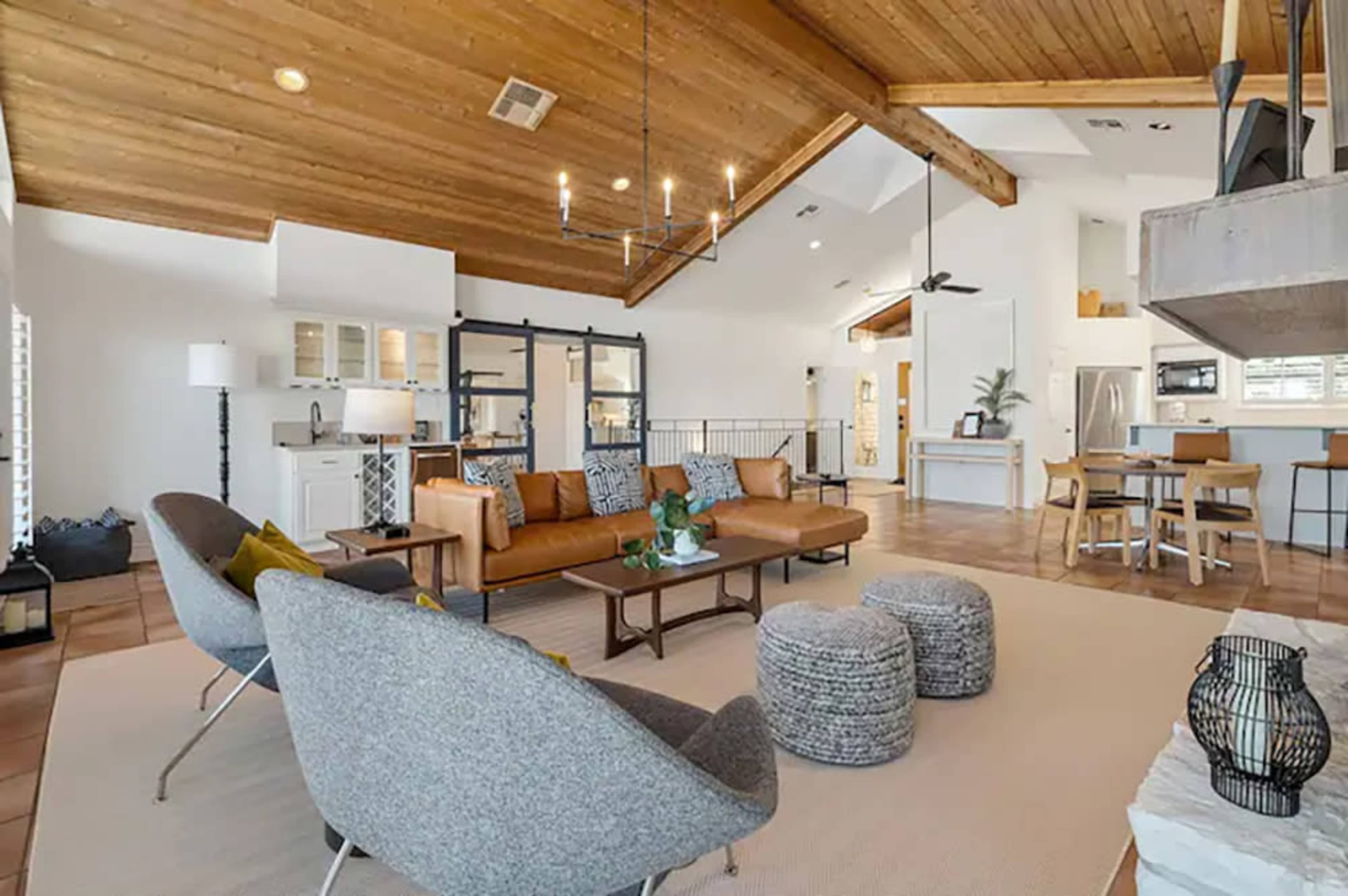 The image depicts a spacious, modern living room with vaulted wood ceilings, a sofa, and a dining area connected to a kitchen.