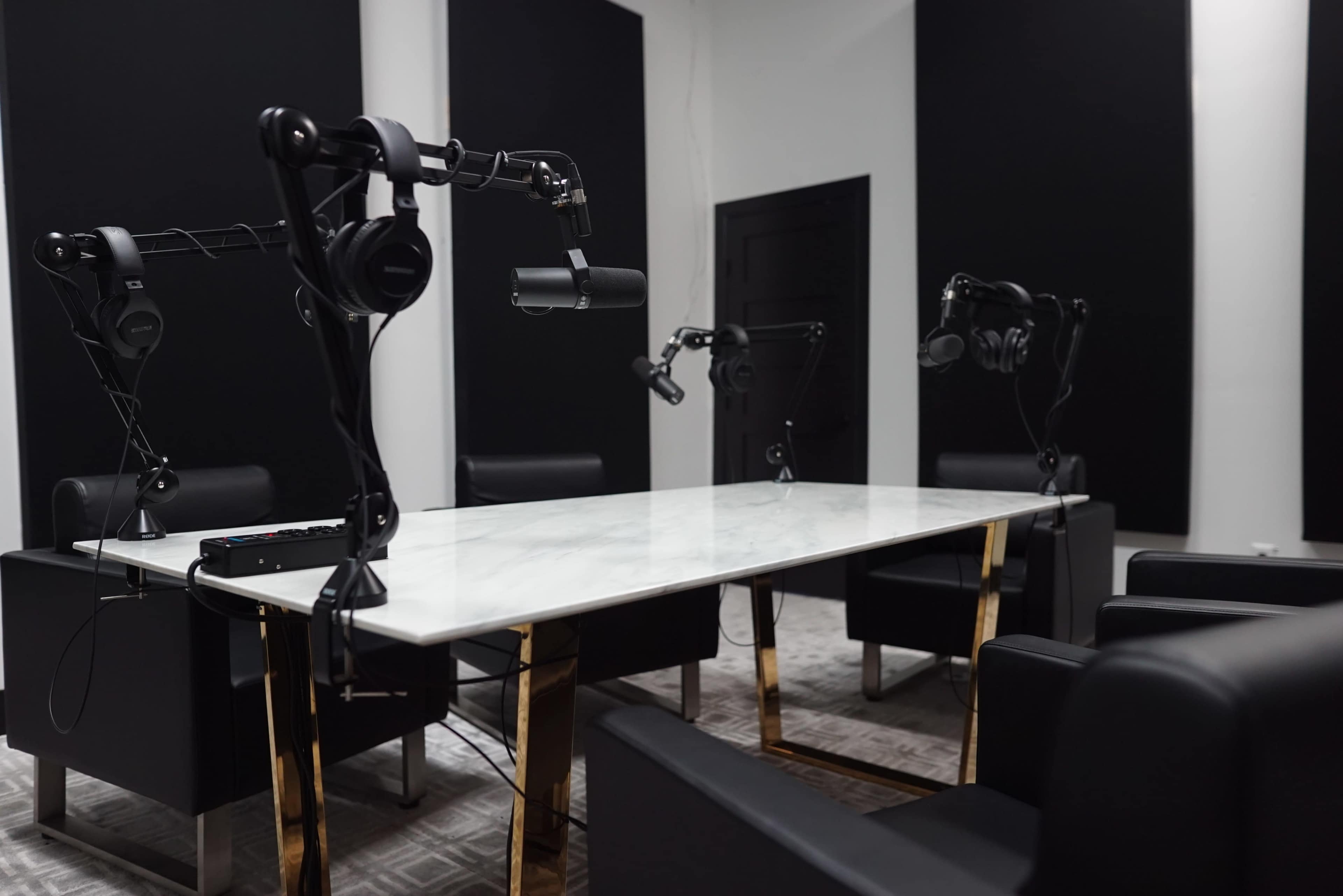 A podcast studio featuring a marble table surrounded by black chairs, with microphone stands and headphones positioned for recording.