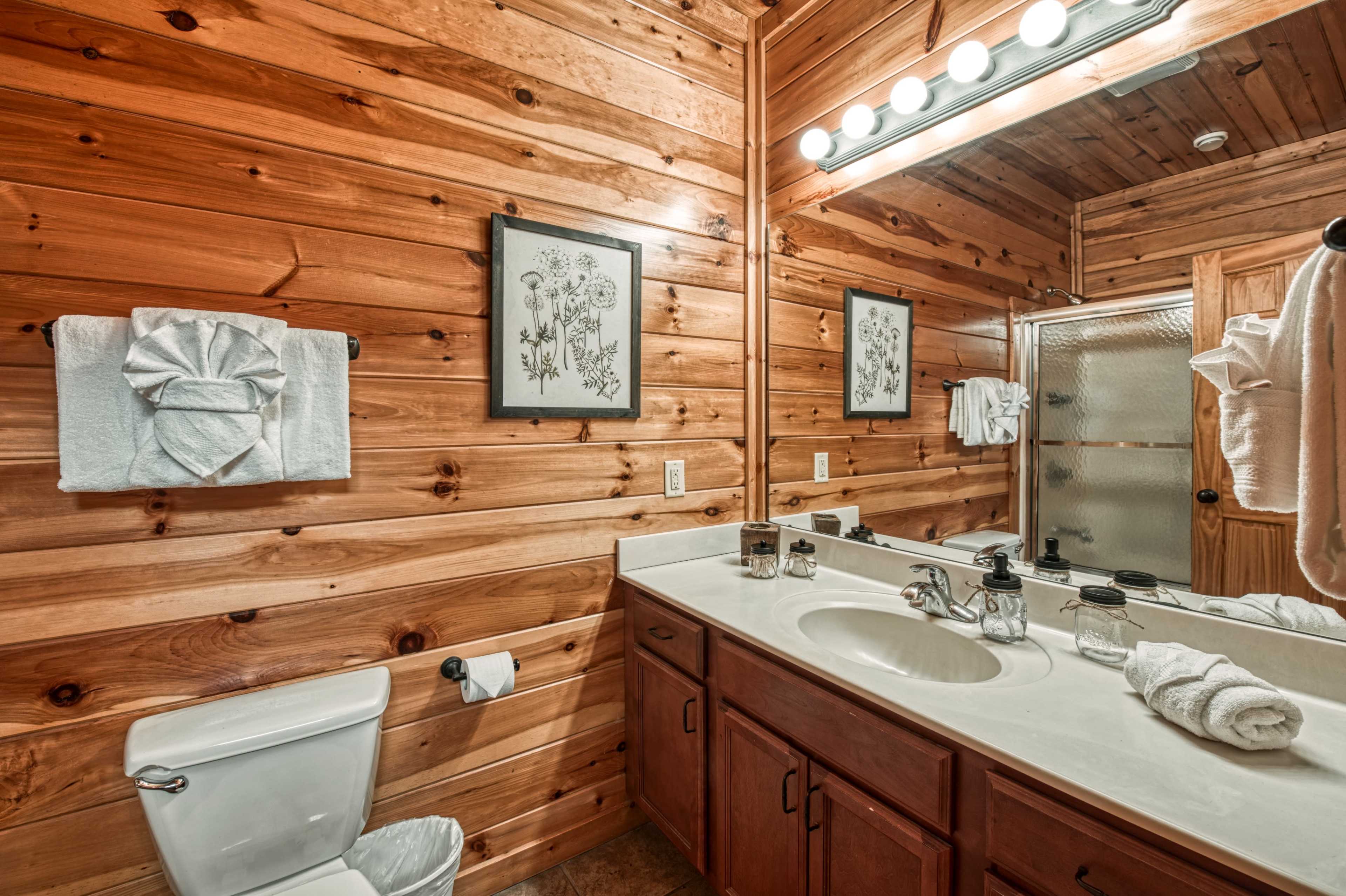 A bathroom features a wooden wall, a double sink vanity with decorative wall art, and a shower stall with glass doors.