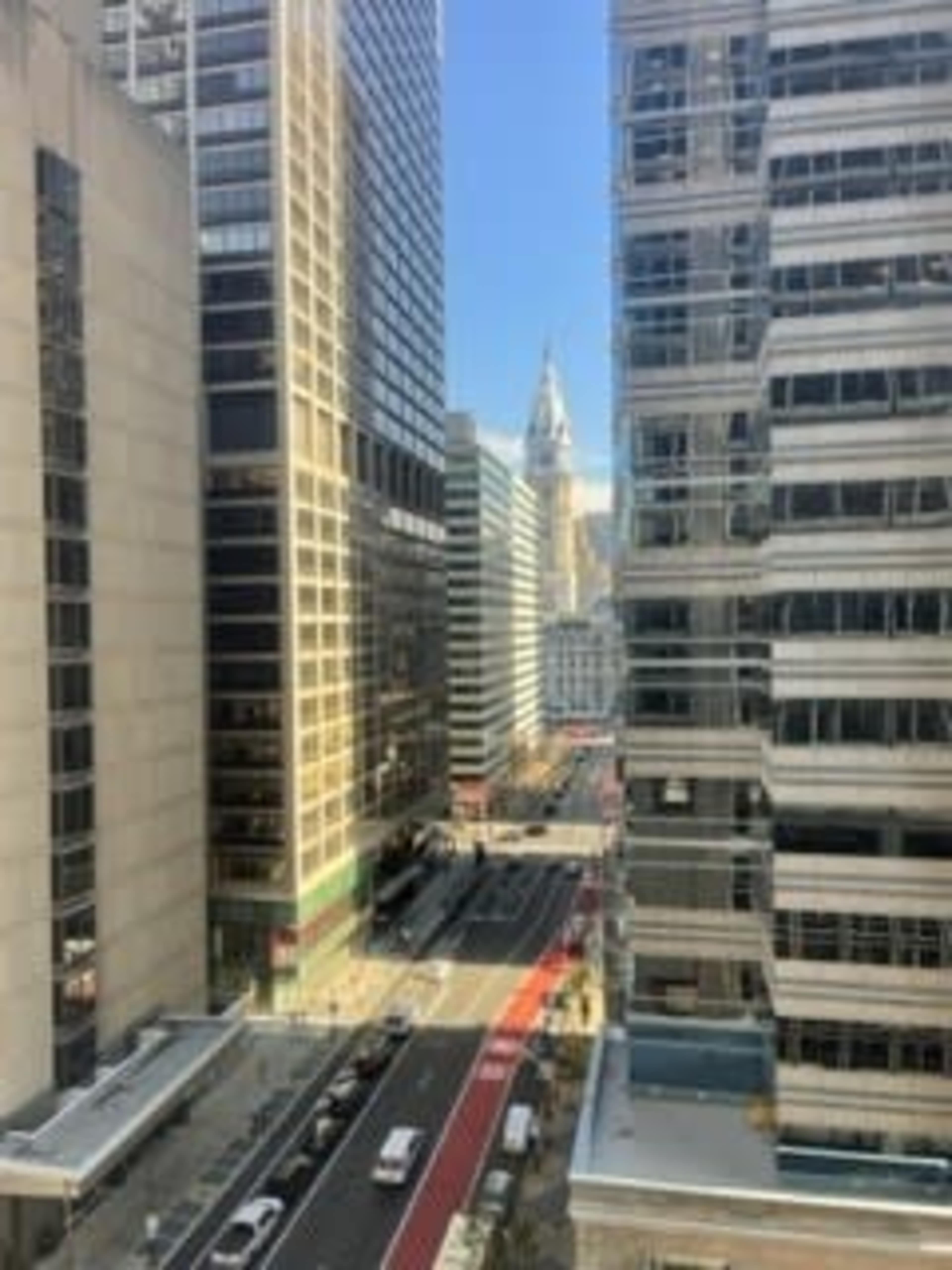 The image shows a city scene with tall buildings lining a street that features light traffic and a visible clock tower in the distance.