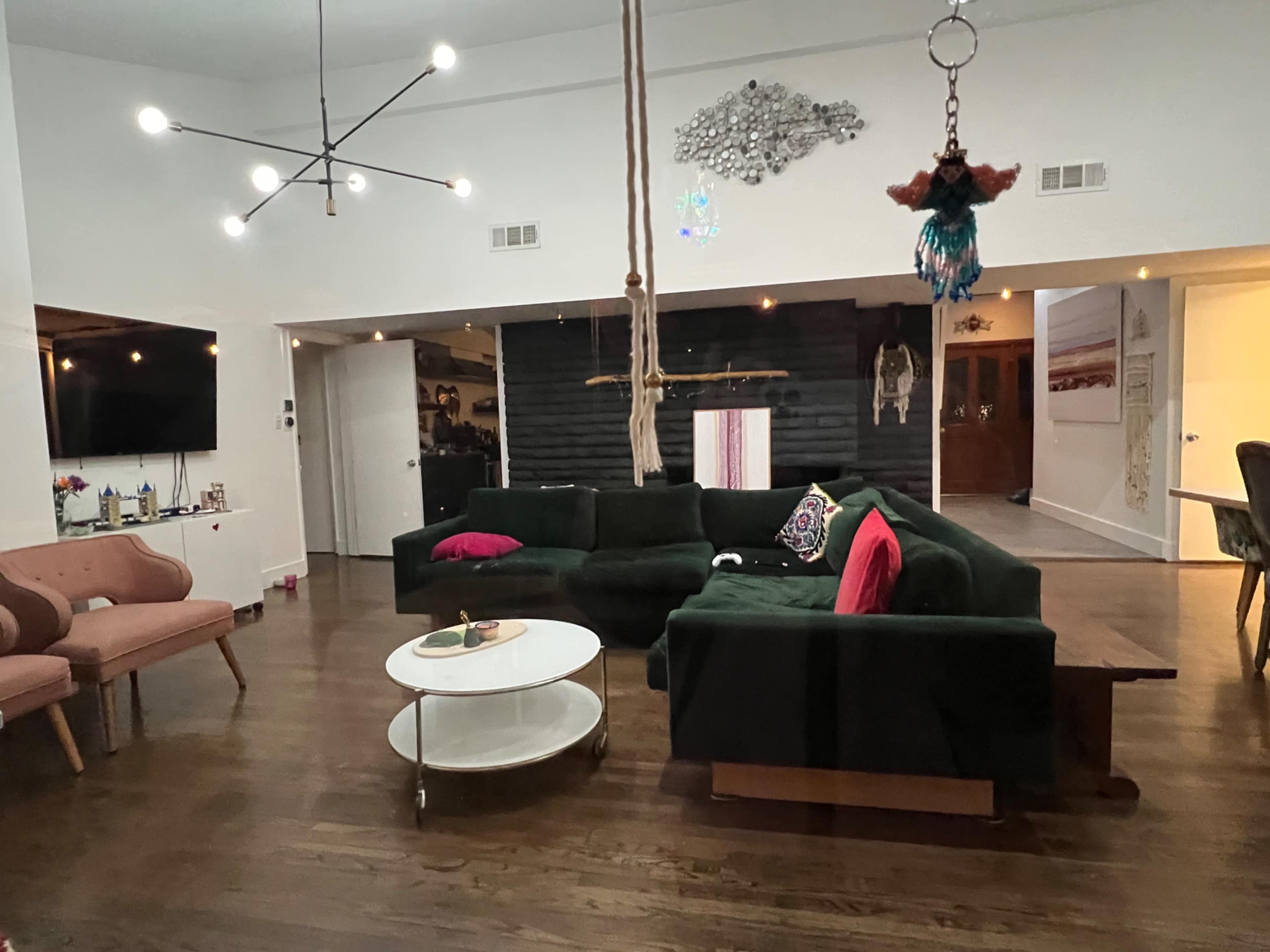 A modern living room featuring a green sectional sofa, a round coffee table, a hanging swing, and a television mounted on the wall.