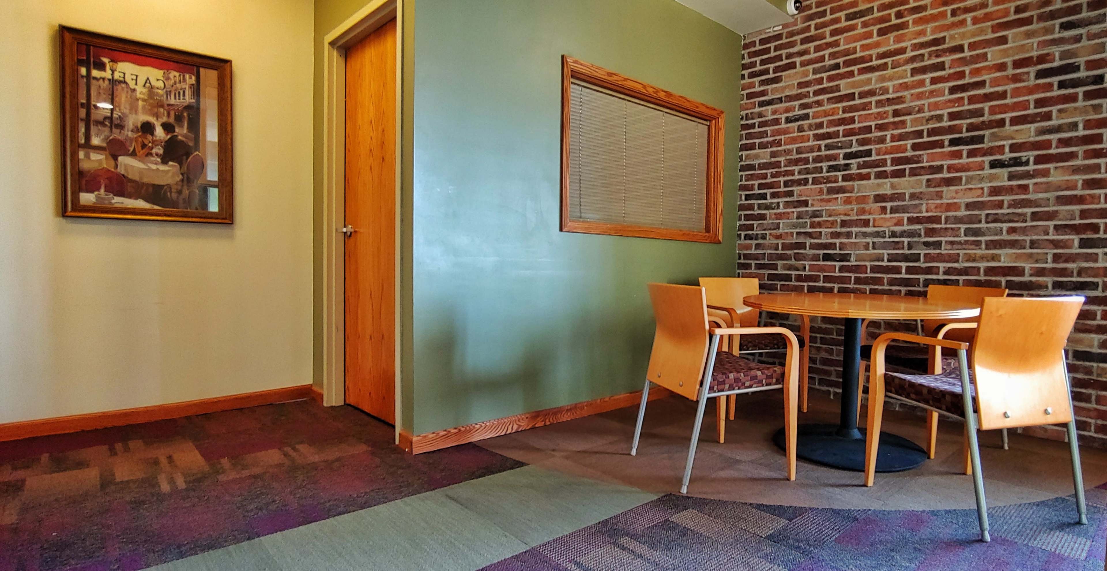 A corner of a room featuring a wooden table with two chairs, a brick wall, and an adjacent door.