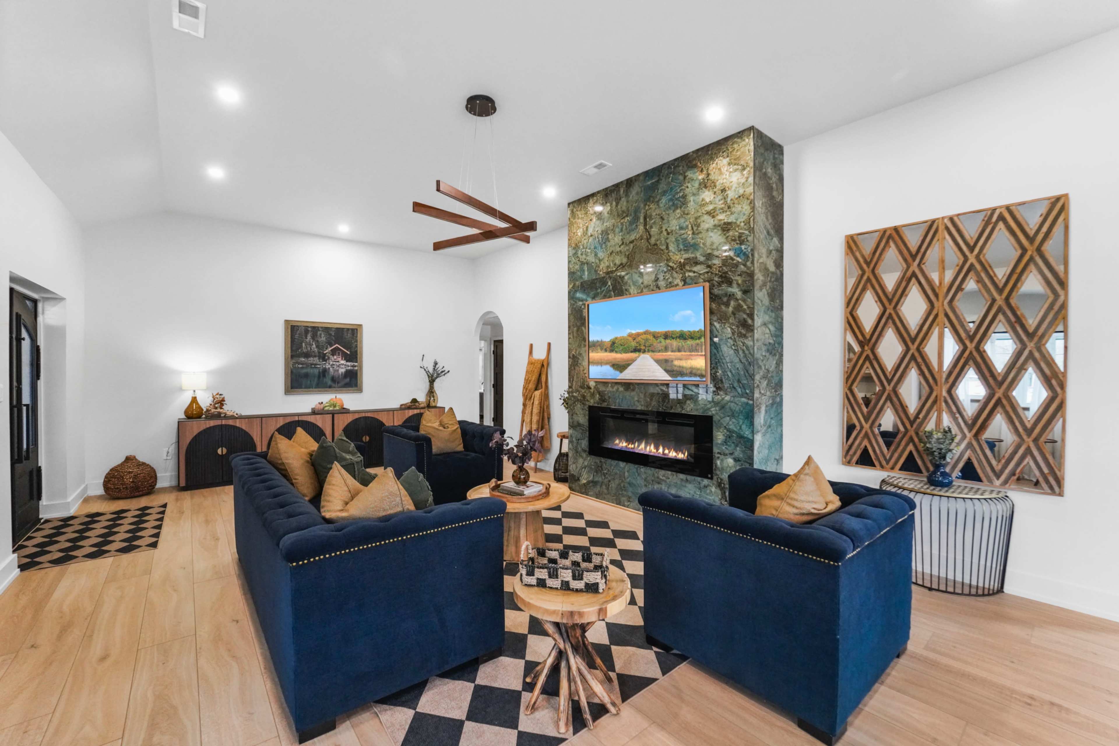 The living room features a cozy arrangement of blue velvet sofas, a modern fireplace, and a large wall-mounted TV, with wooden accents and a decorative mirror.