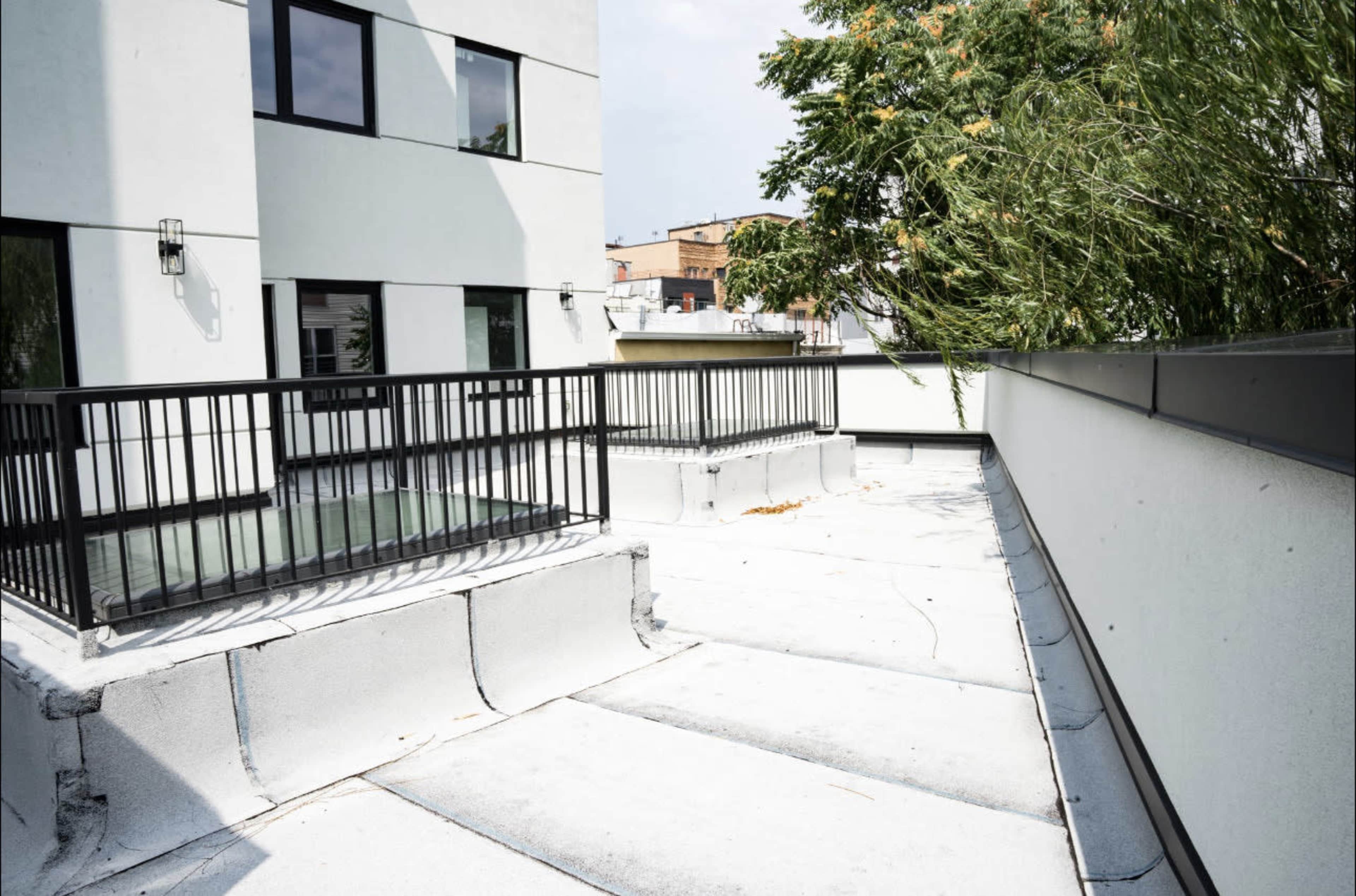 A rooftop space with a railing, a flat surface, and nearby buildings in the background.