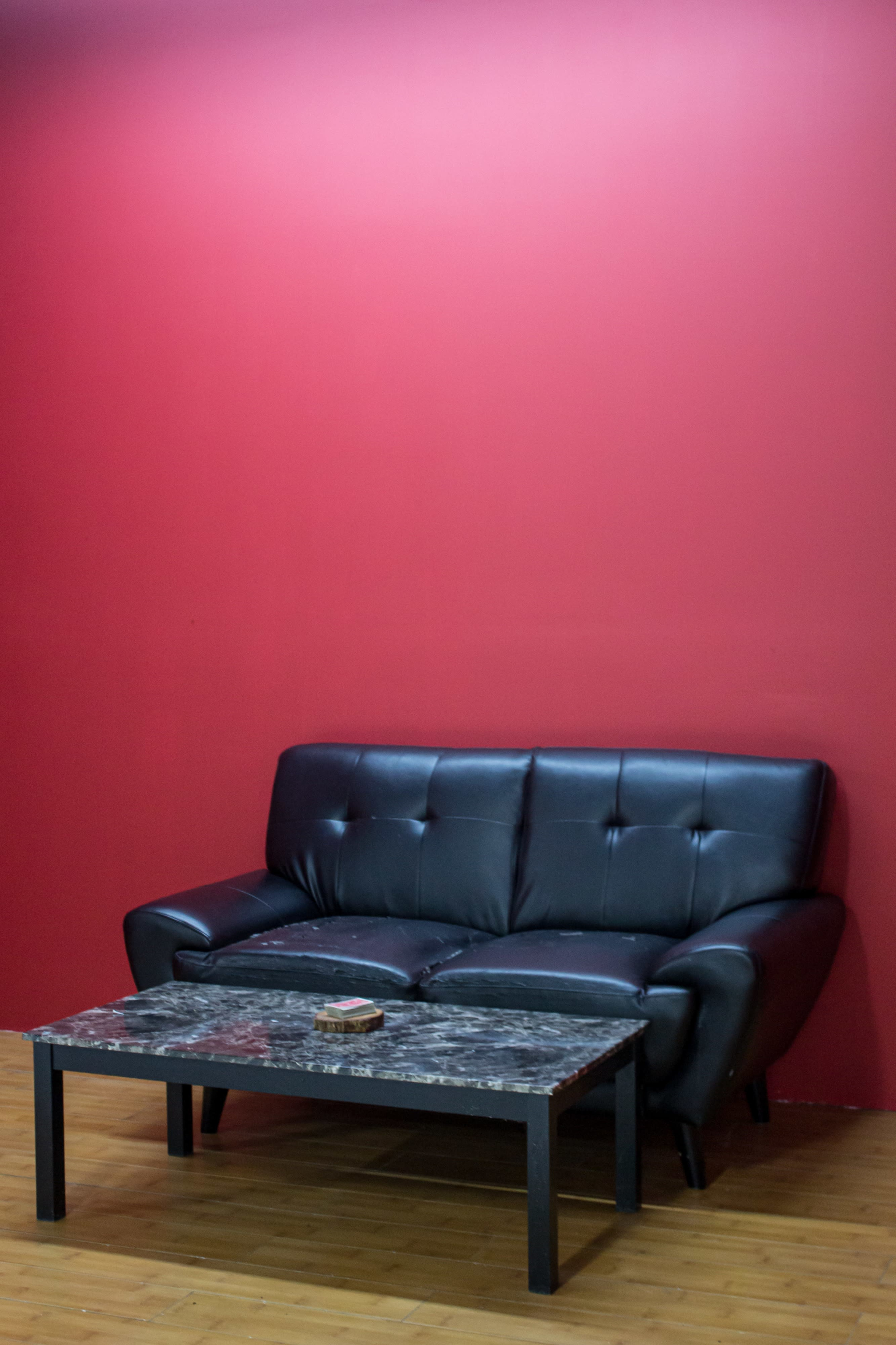 A black leather couch is placed in front of a red wall, accompanied by a marble-top coffee table.