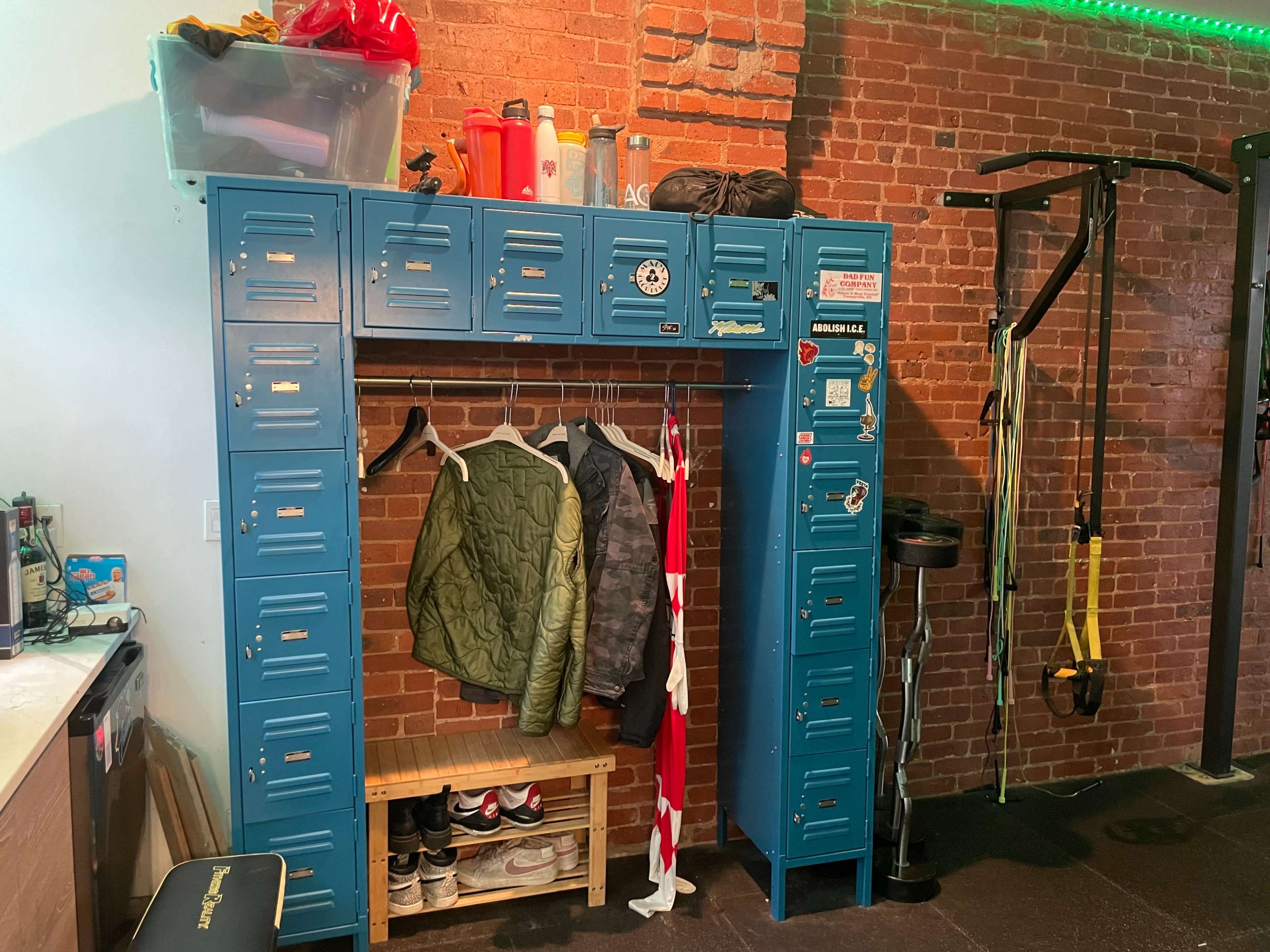A blue locker unit with multiple compartments, a wooden bench below, and several items such as clothing, bags, and workout equipment nearby in a fitness space.