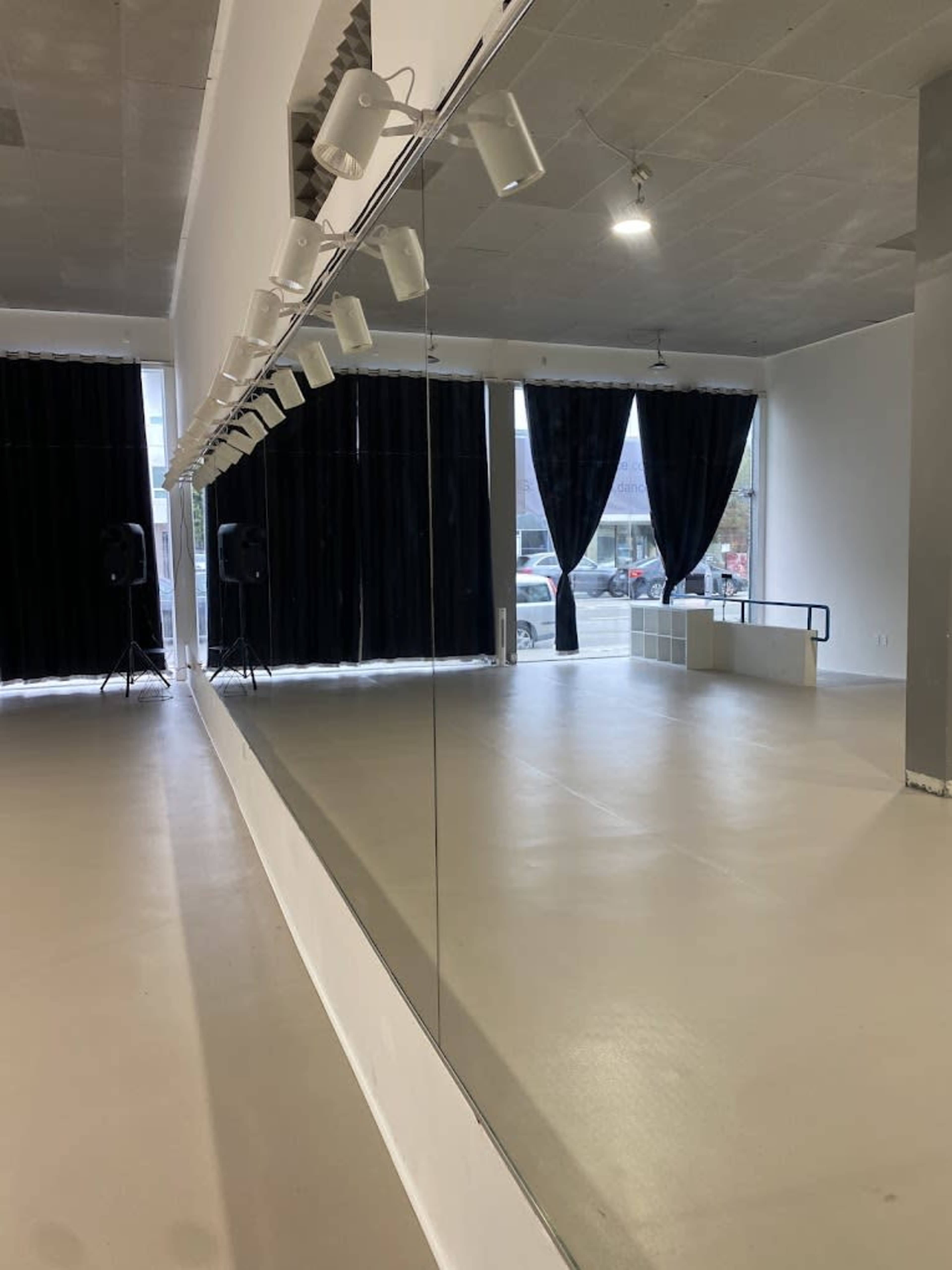 A dance studio features a large mirror along one wall, with black curtains covering the windows and speakers positioned in the corners.