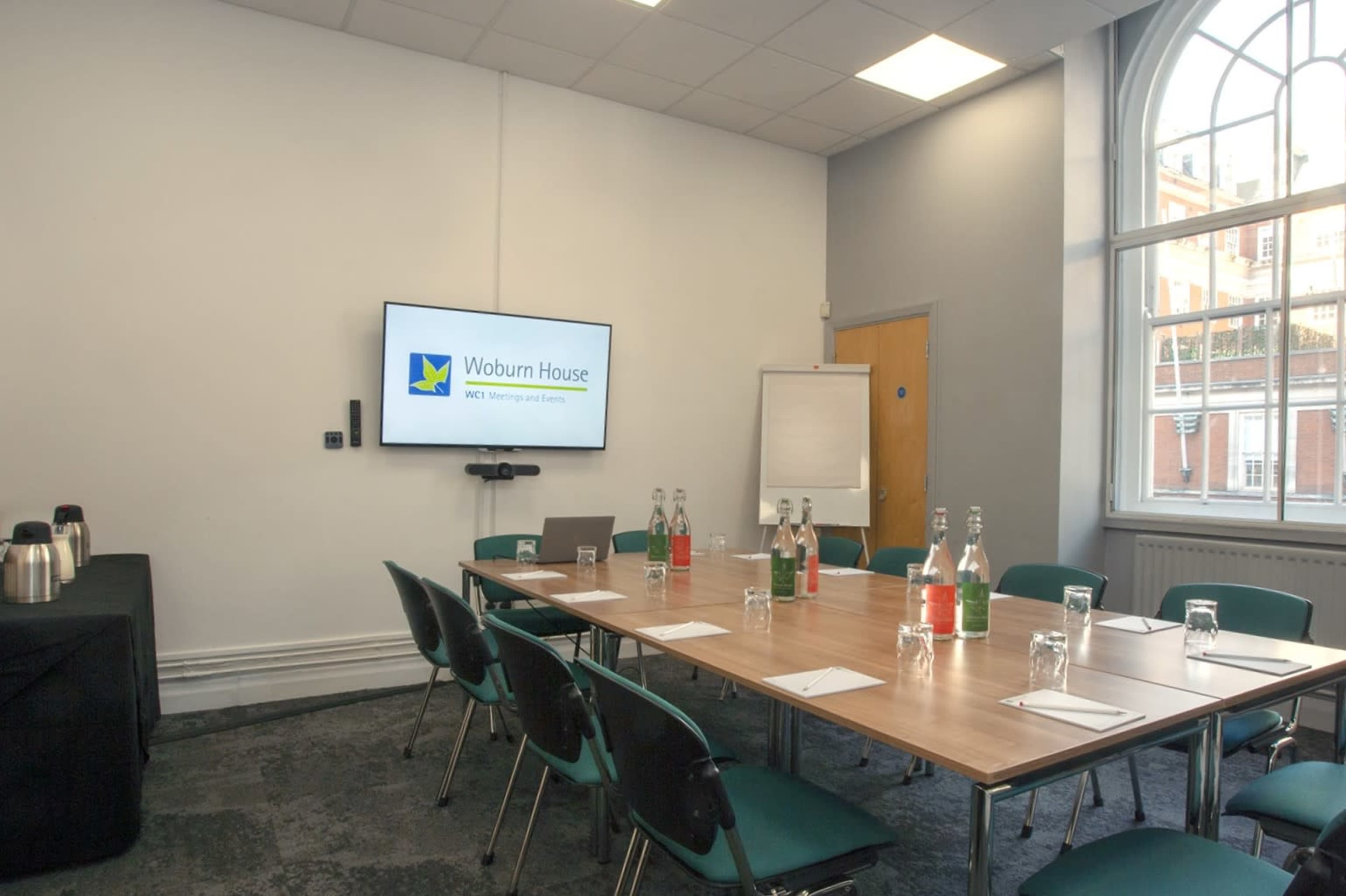 A meeting room is set up with a large table, chairs, a presentation screen, and water bottles.