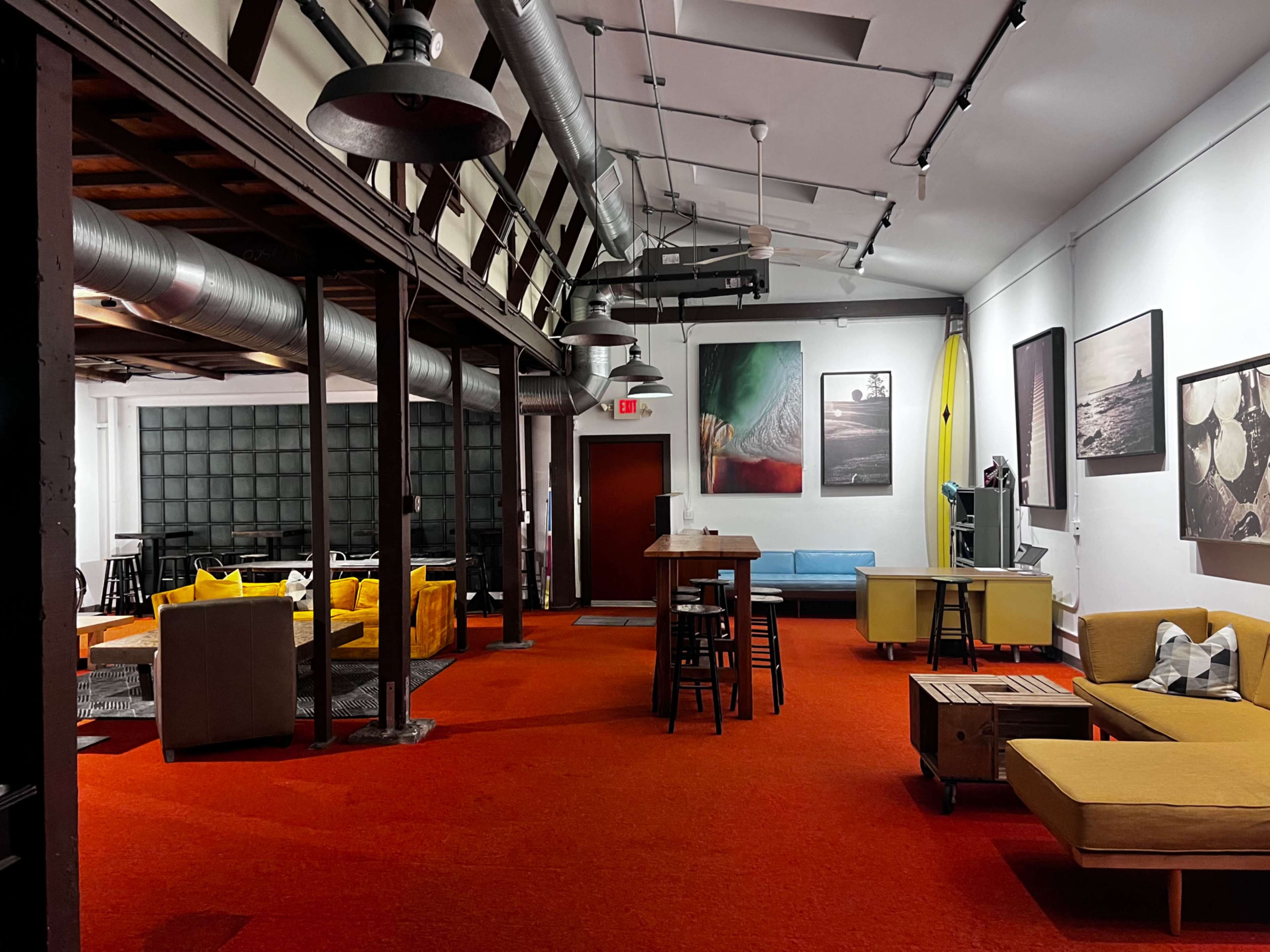 The image shows a spacious indoor lounge area with red carpet, various seating arrangements, and modern decor featuring art on the walls.