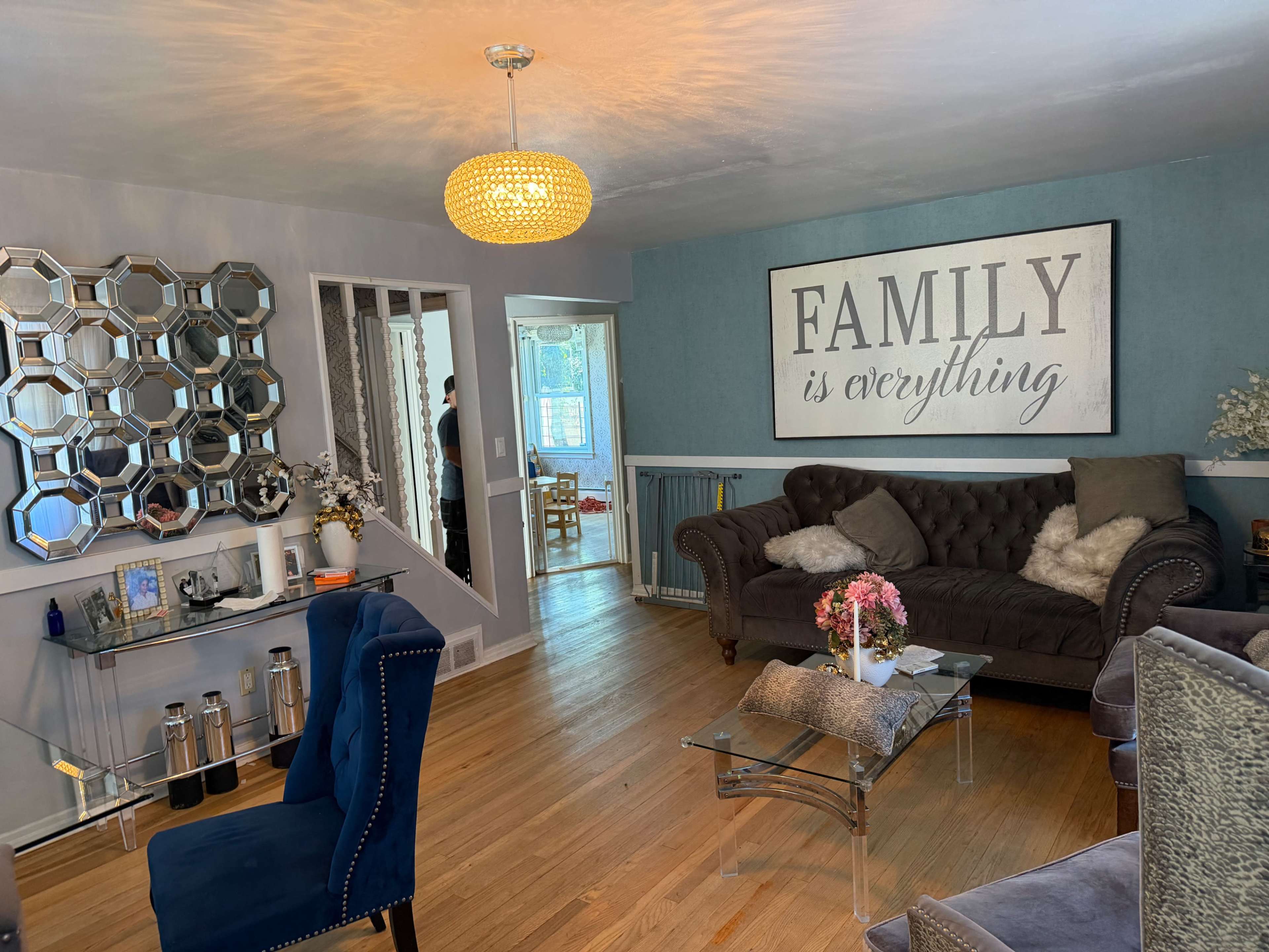 The living room features a blue wall with a large framed sign that reads "FAMILY is everything," a brown sofa, a glass coffee table, and decorative accents.