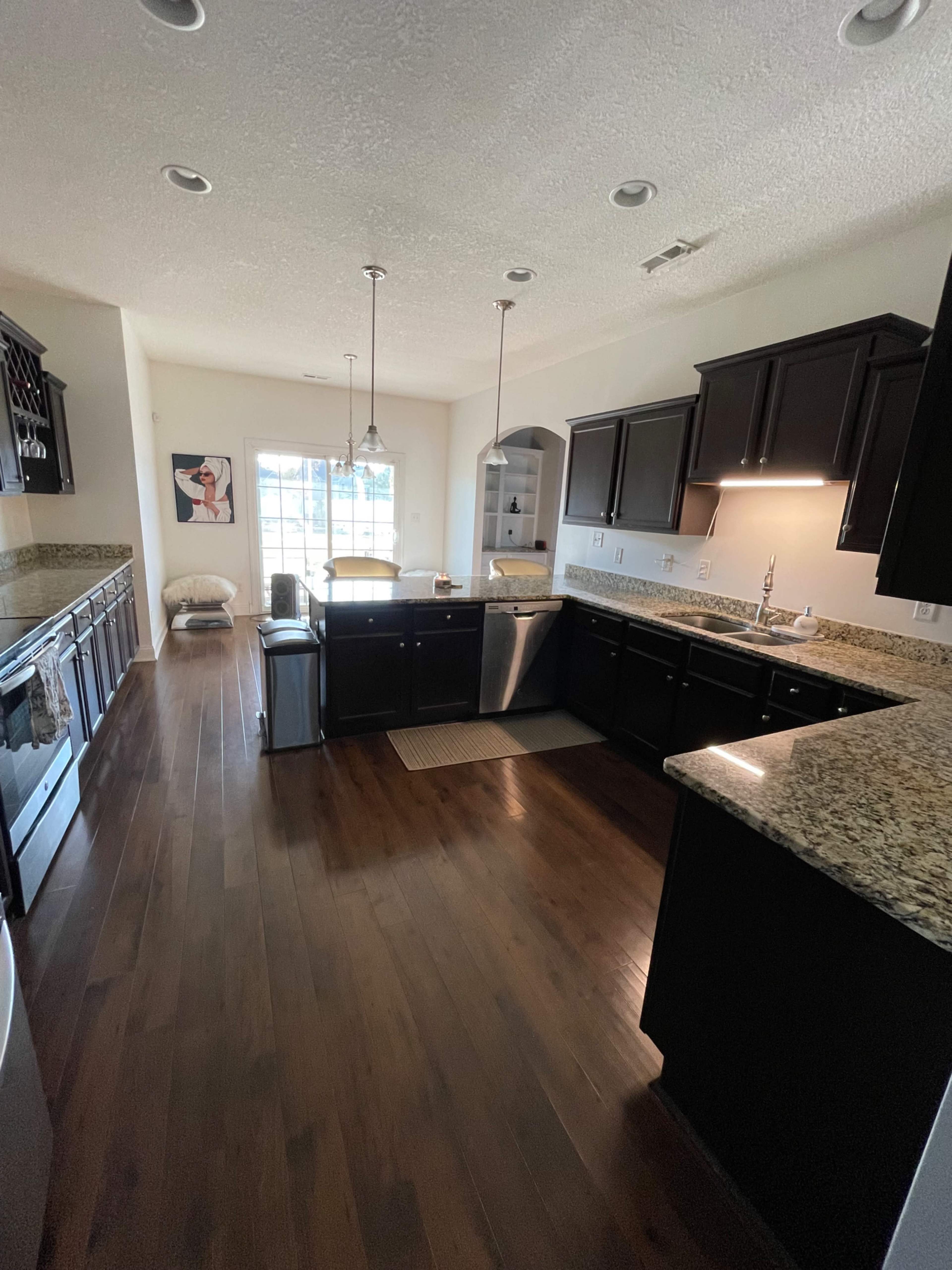 A spacious kitchen features dark wooden cabinetry, granite countertops, and a large window allowing natural light to fill the room.
