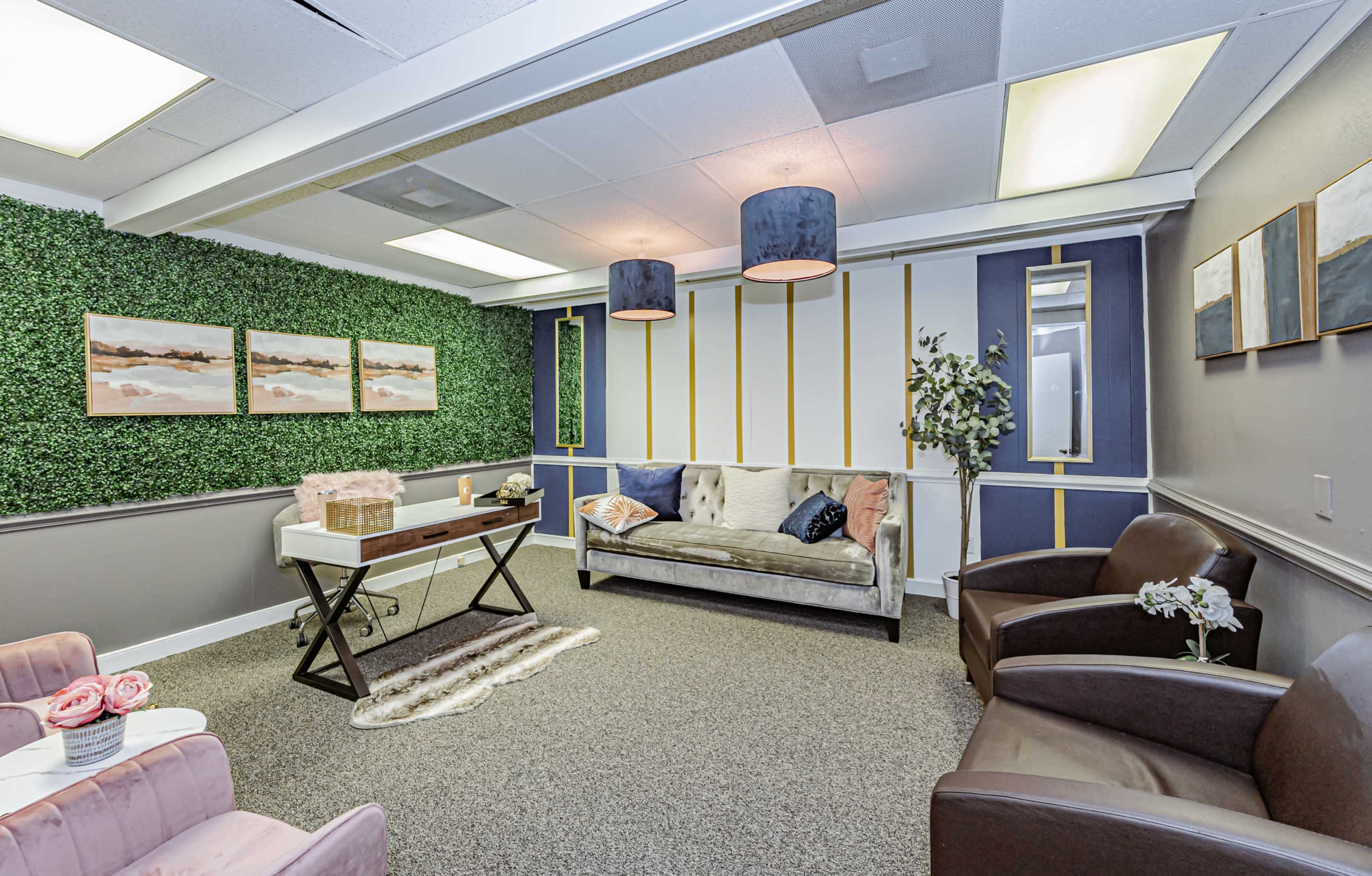 A modern waiting room with green wall accents, a gray sofa, two brown chairs, and decorative artwork hanging on the walls.