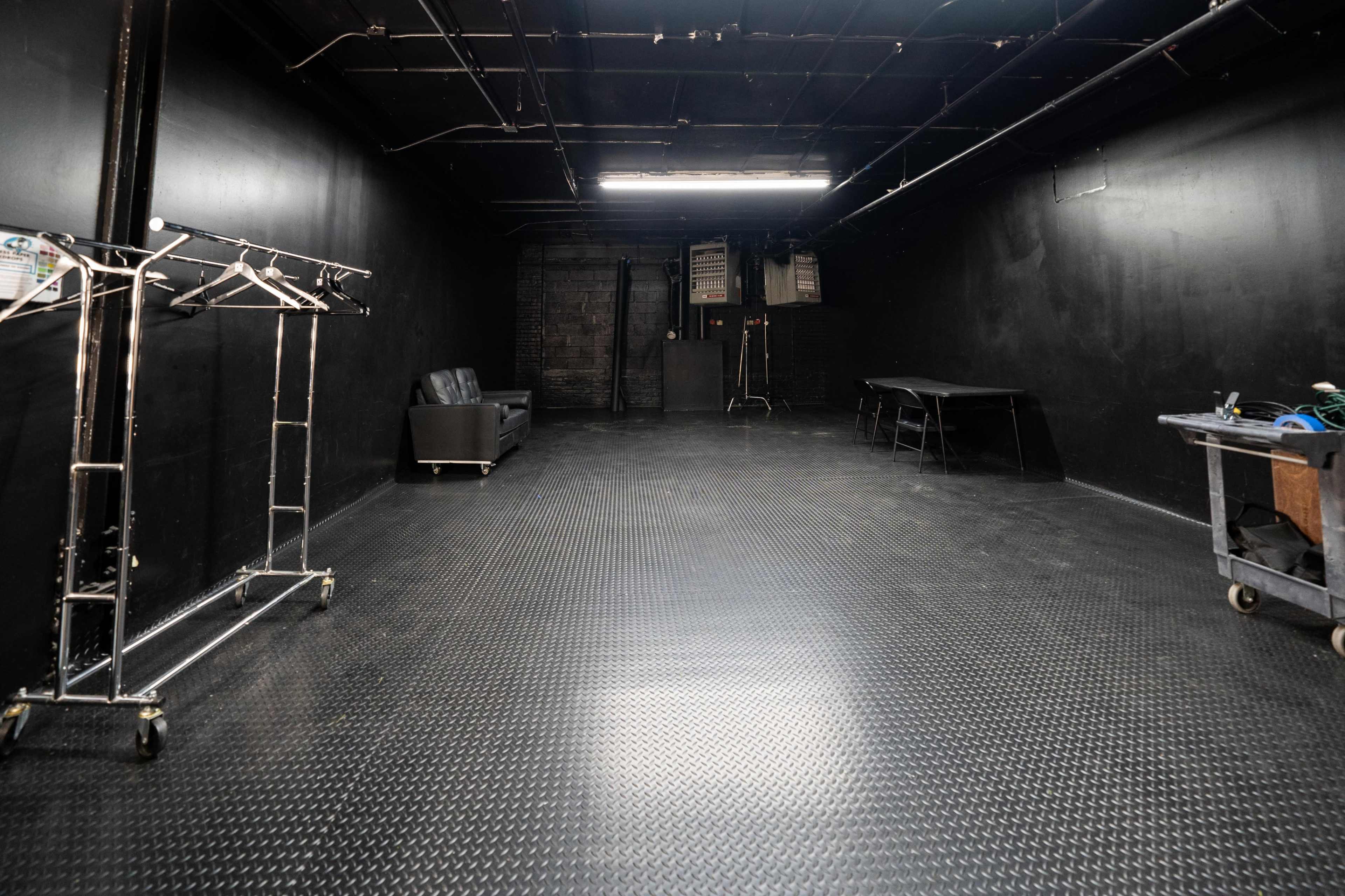 An empty black-walled studio space features a couch, a table, and clothing racks against the walls.