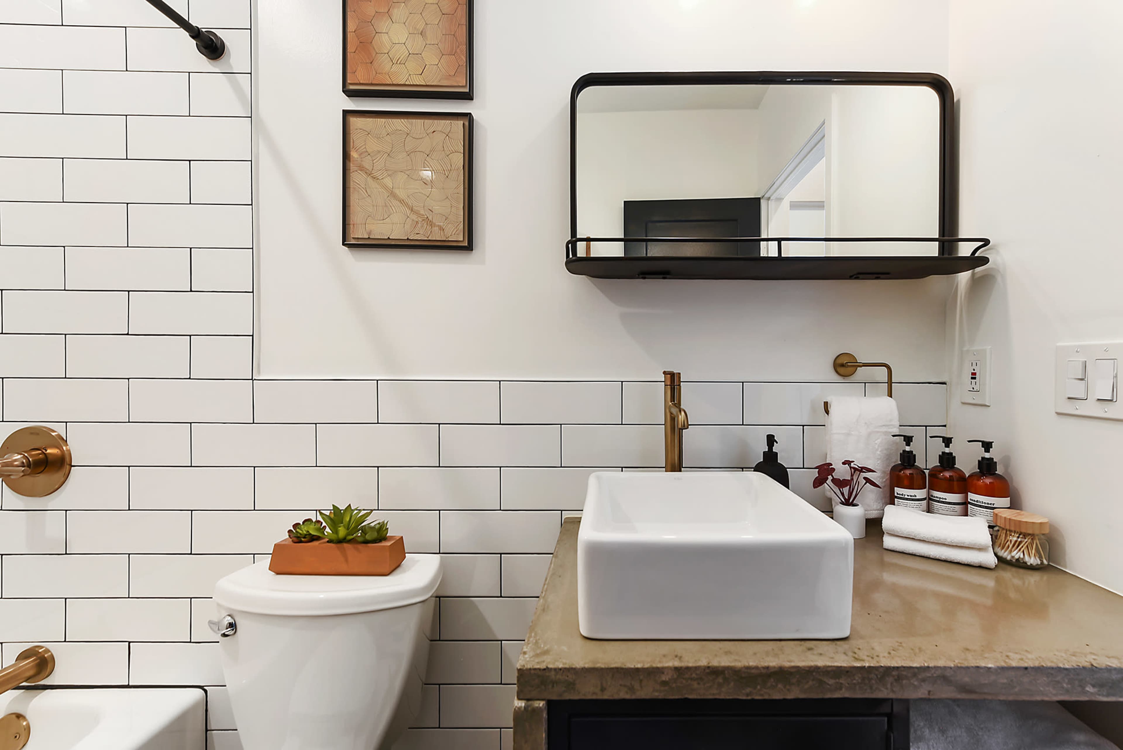 The image shows a bathroom featuring a white rectangular sink, a wall-mounted mirror, and a toilet beside a tiled wall.