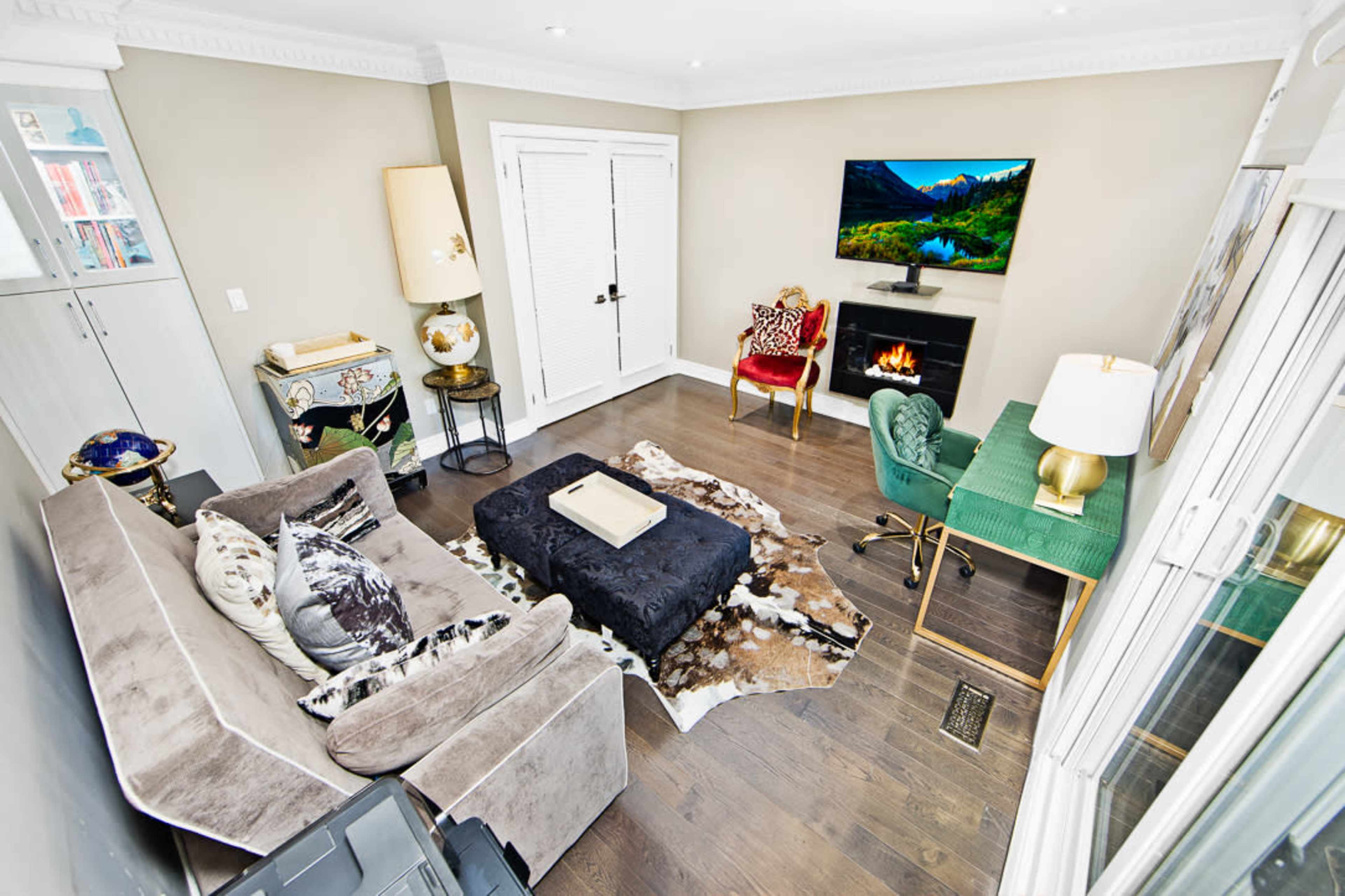 The image shows a modern living room featuring a sofa, a cowhide rug, a fireplace, a television mounted on the wall, and various pieces of furniture, including a green chair and a lamp.