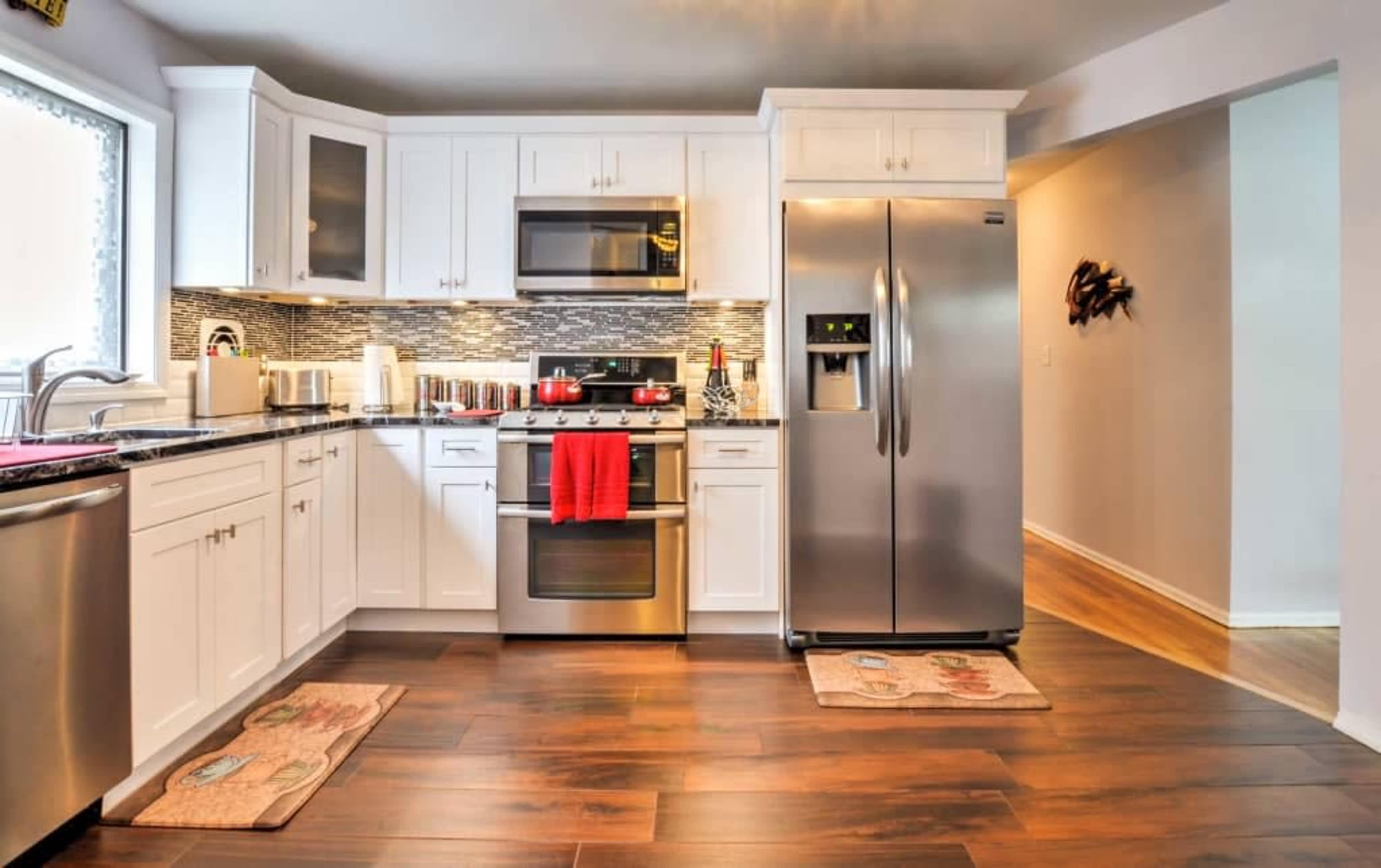 A modern kitchen with stainless steel appliances, white cabinets, and wooden flooring.